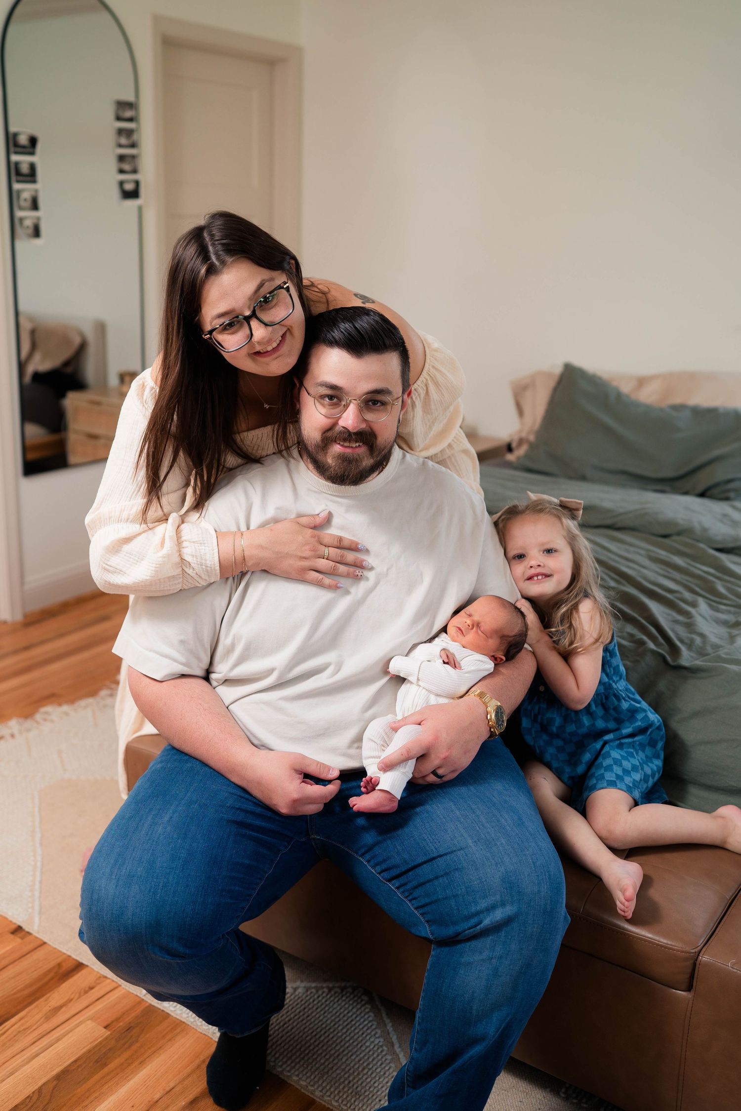 Happy family of four posing together at home, parents with newborn baby and smiling toddler girl.