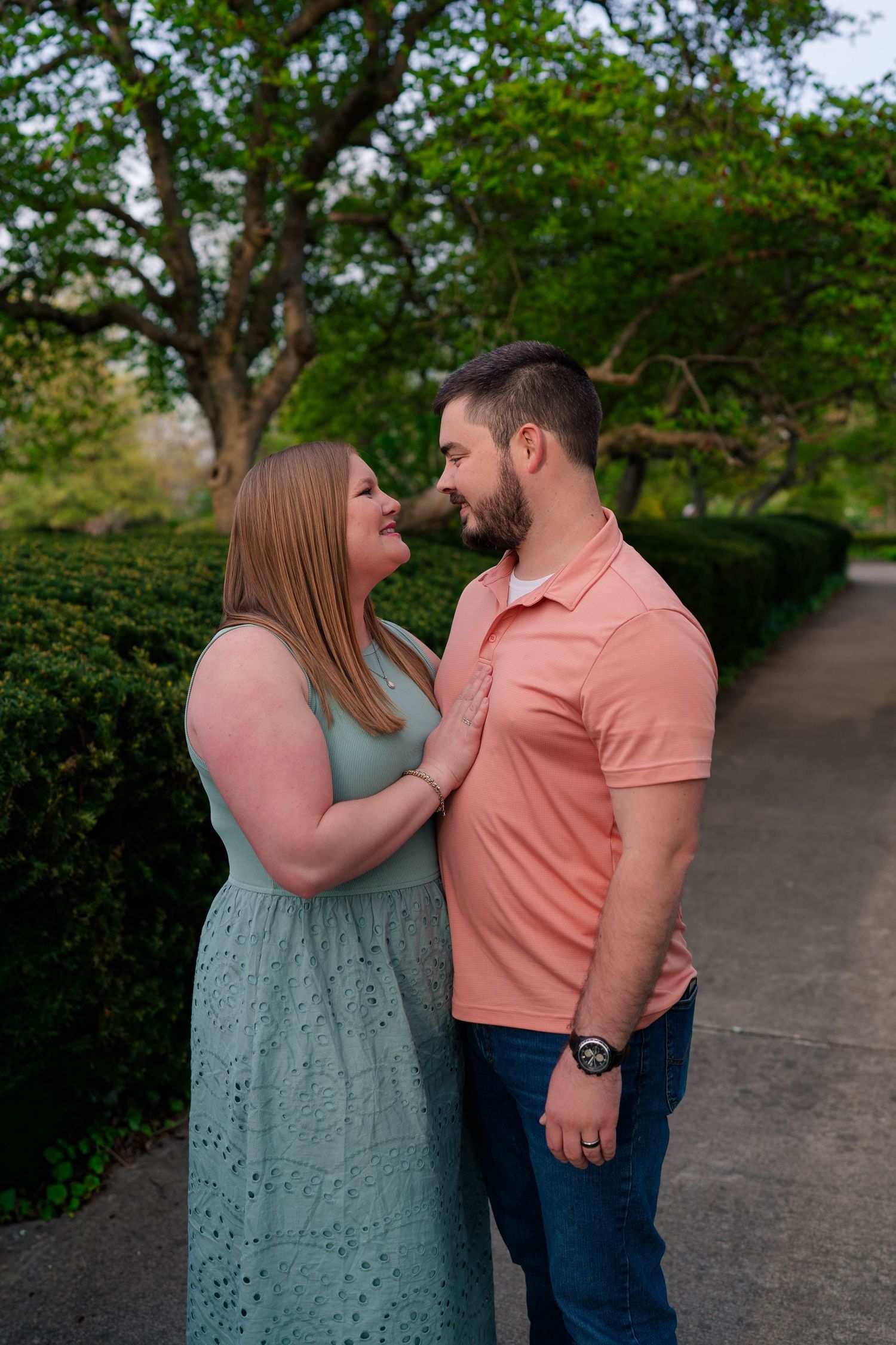 Couple gazes lovingly at each other in a lush green garden, woman in mint dress, man in coral polo shirt.