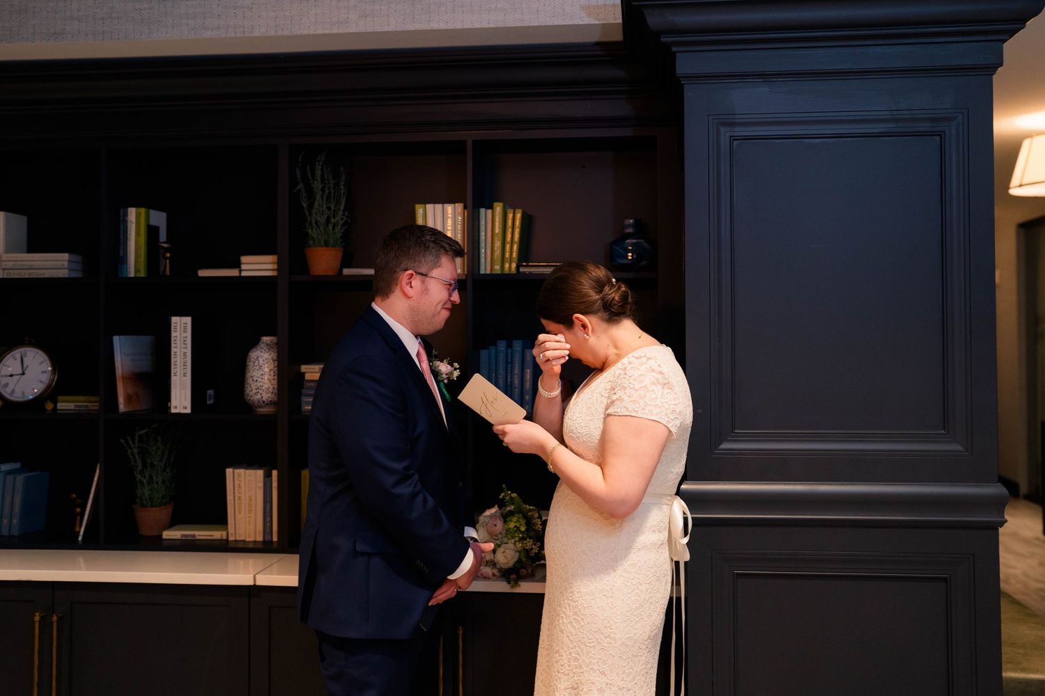 Bride wiping tears of joy as couple shares intimate private vow exchange in elegant library.
