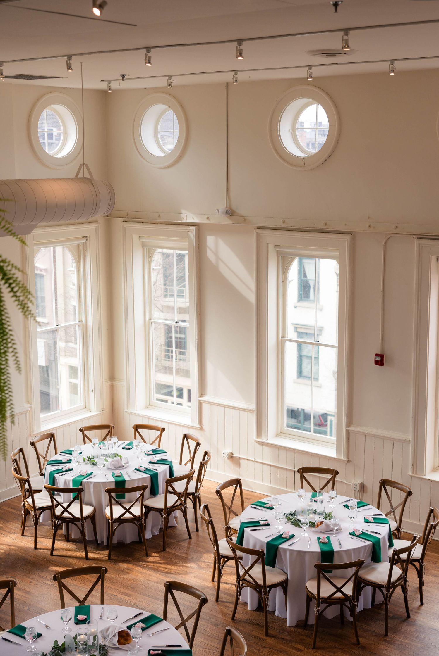 Aerial view of elegant wedding reception venue with round tables, green napkins, white linens, and circular porthole windows.