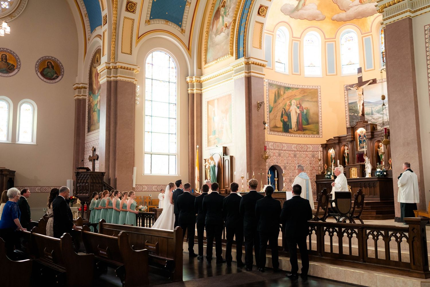 Wedding party stands at the altar of a beautiful Catholic church with blue and gold architectural details.