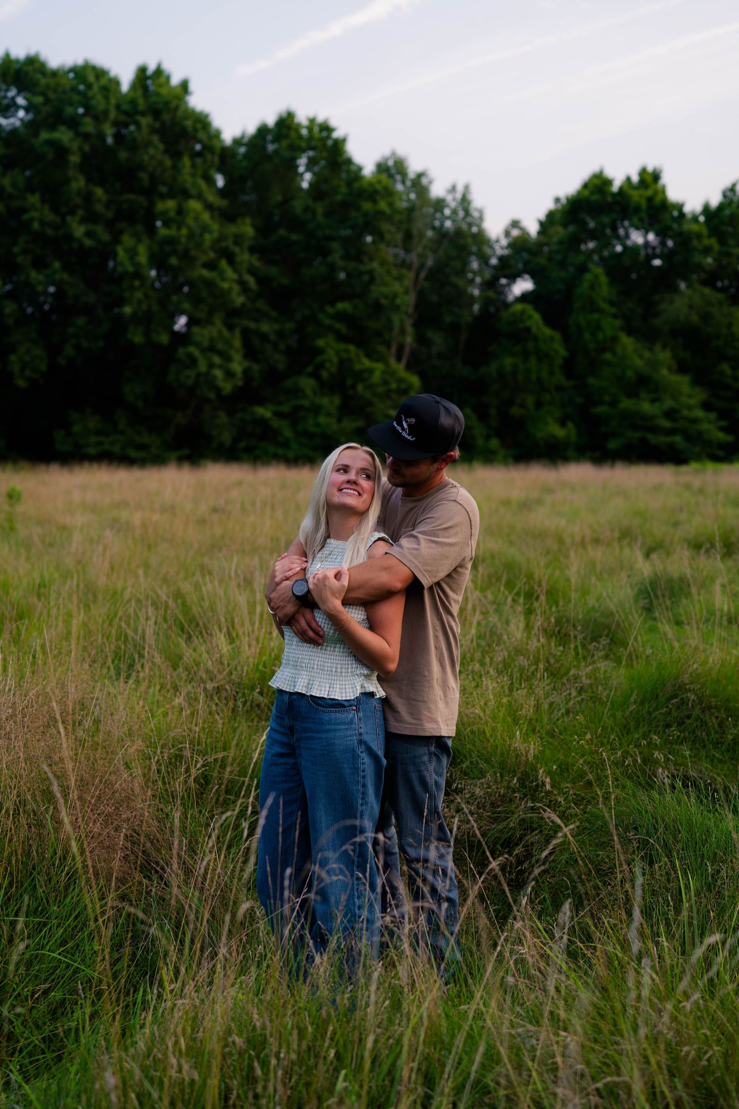 Happy couple embracing in a lush green meadow at dusk, woman smiling joyfully.
