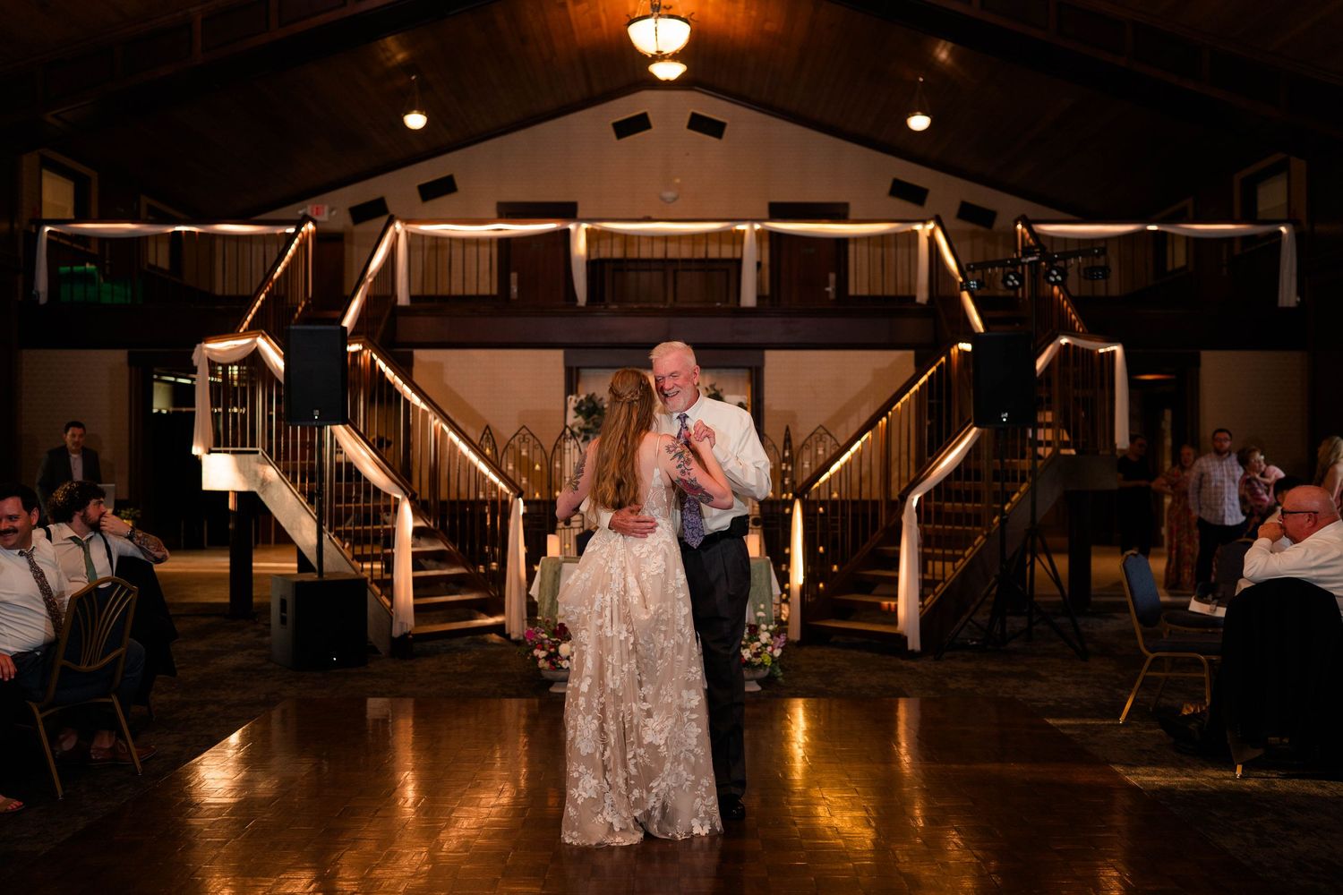 Bride and father share emotional father-daughter dance in grand rustic wedding reception hall.
