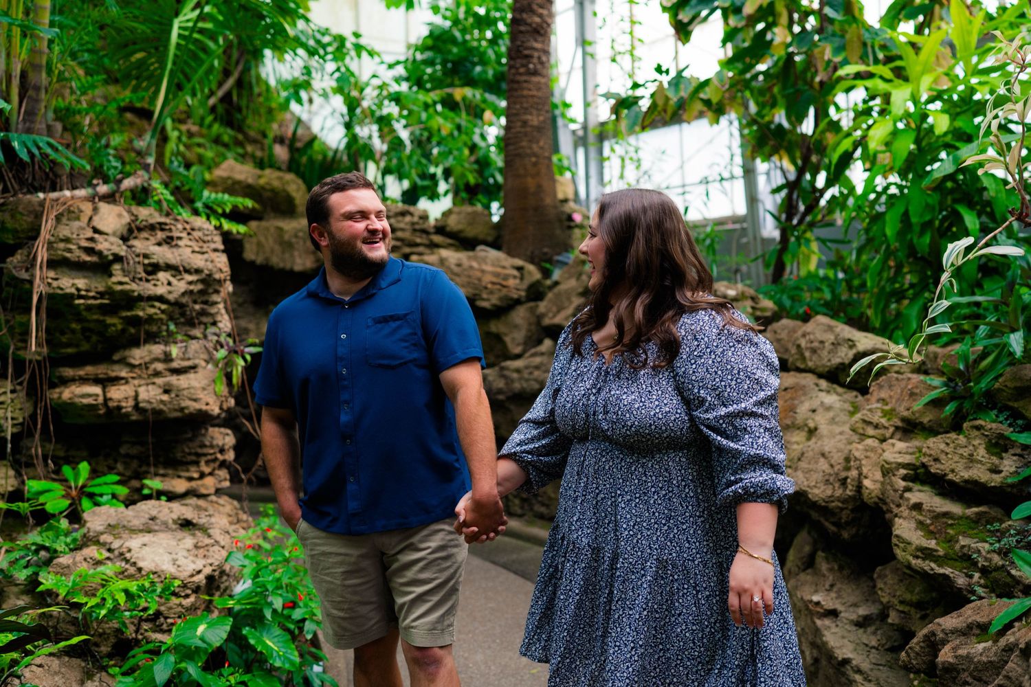 Couple holding hands and smiling at each other on a path through a tropical conservatory.