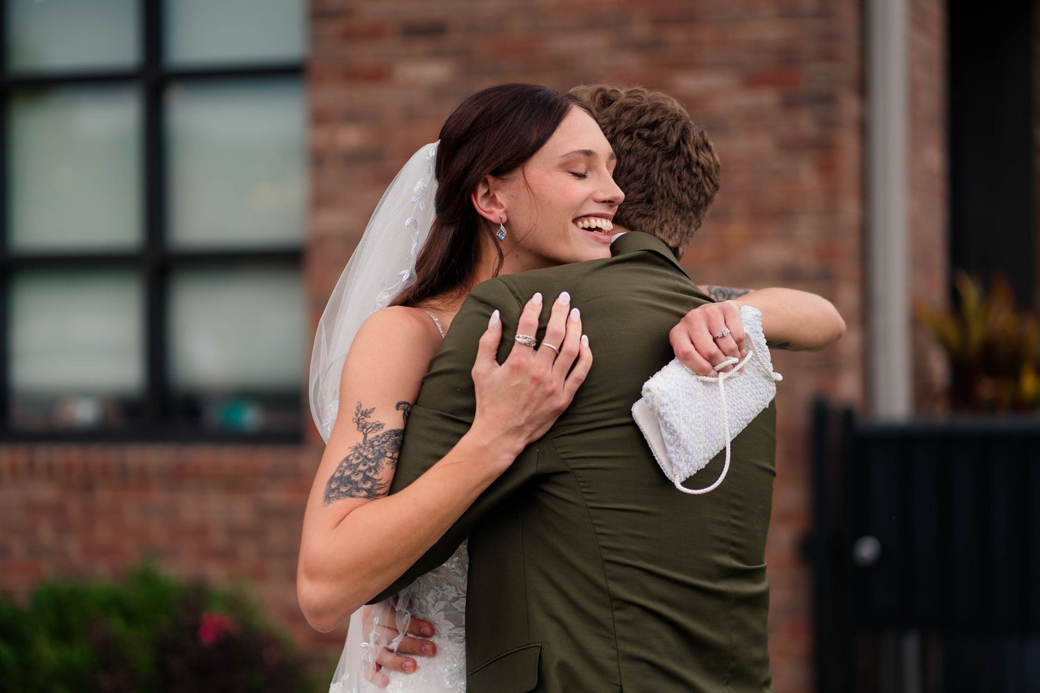 Bride in white dress and veil hugging a guest outdoors at a wedding celebration.