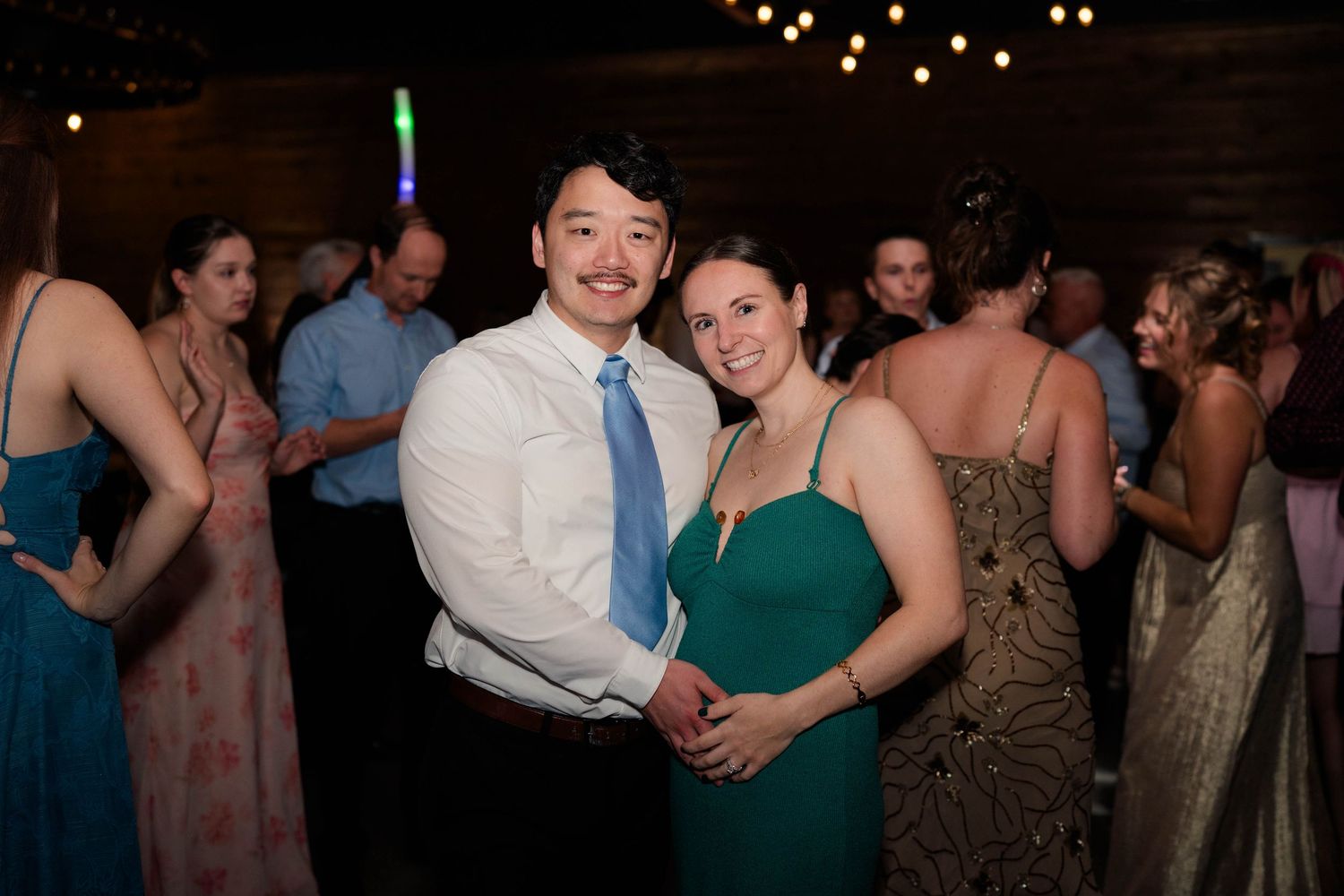 Couple in teal dress and blue tie embrace and smile on the wedding dance floor.