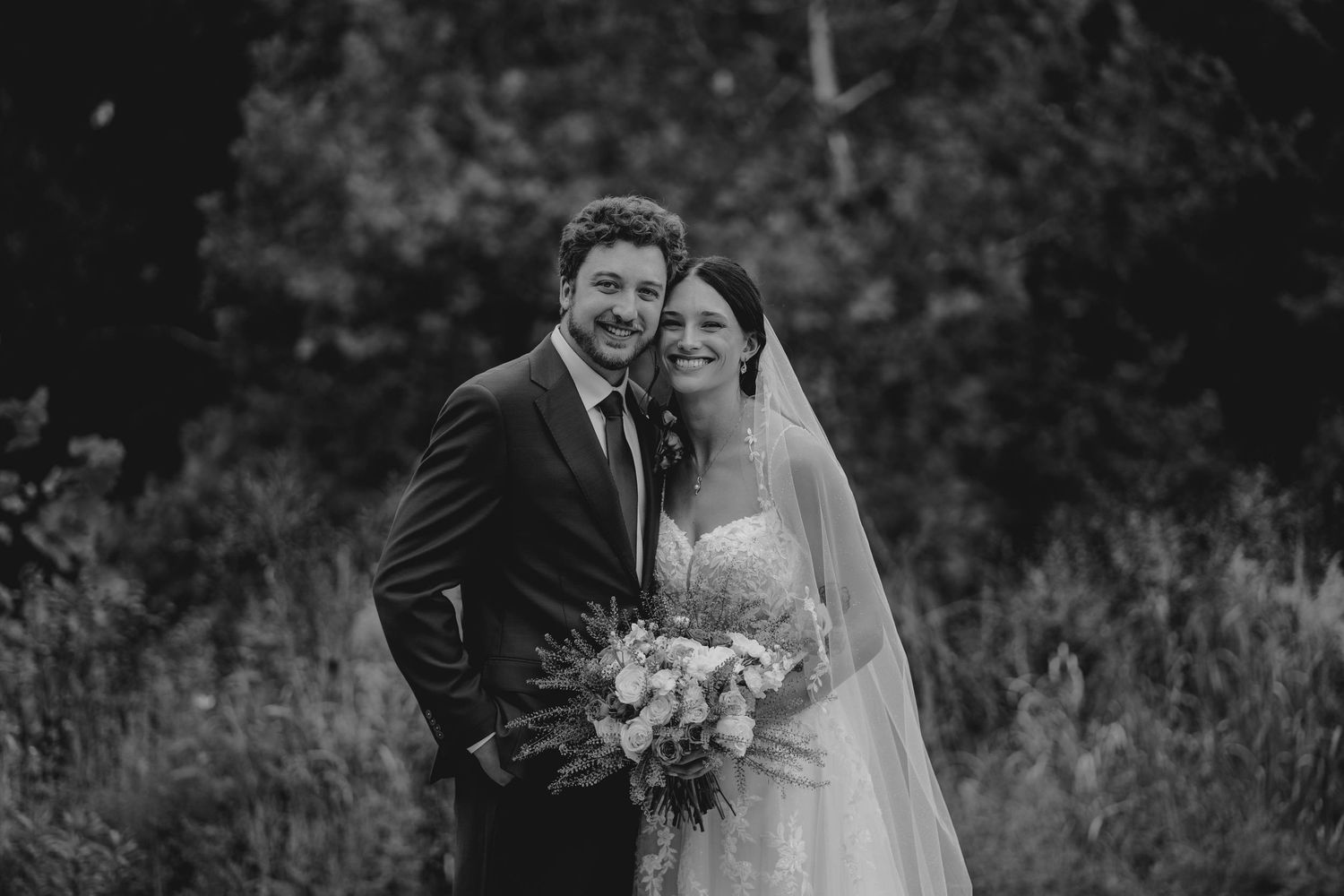 Black and white portrait of smiling bride and groom outdoors on their wedding day.