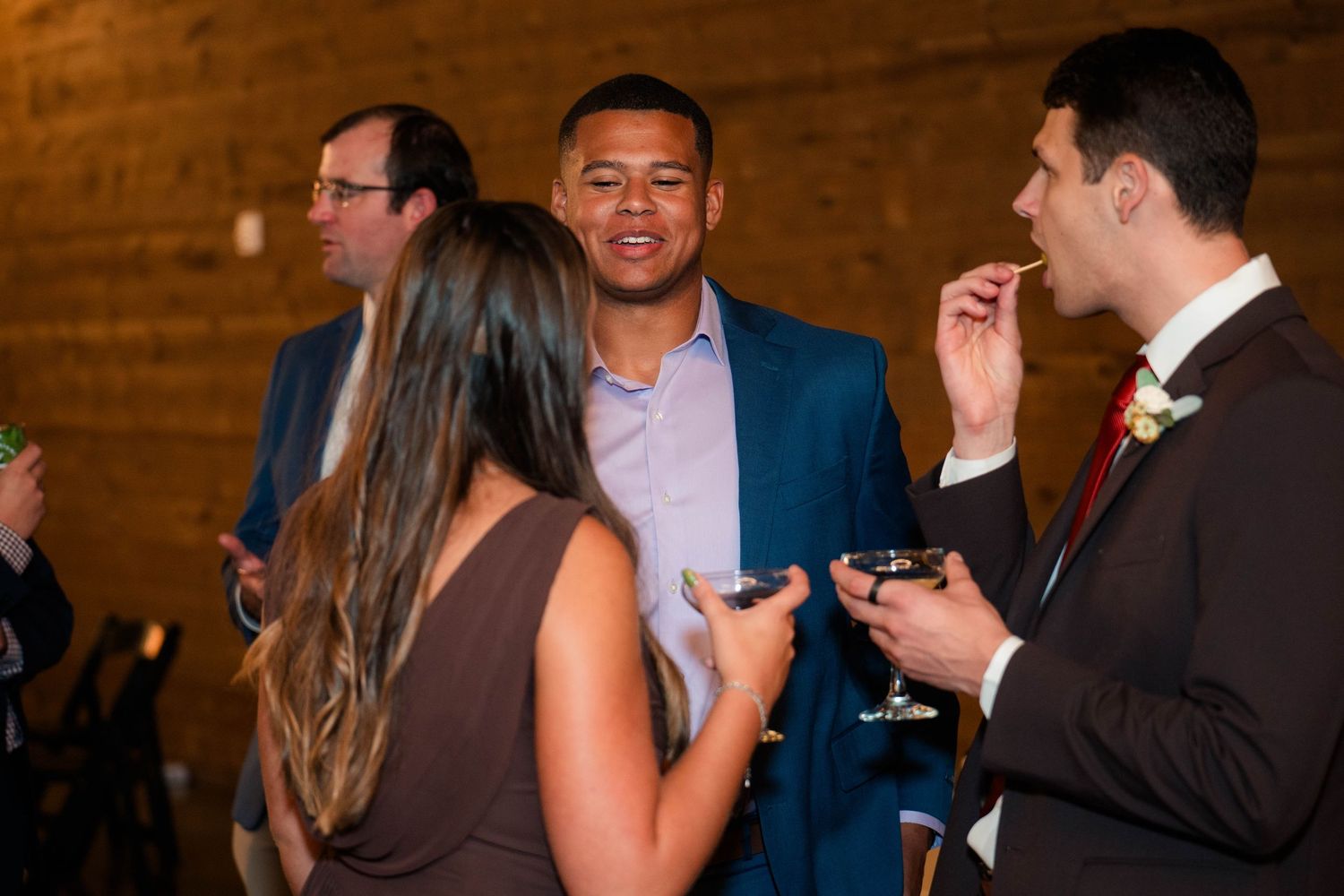 Wedding guests socializing and laughing together during a reception cocktail hour indoors.