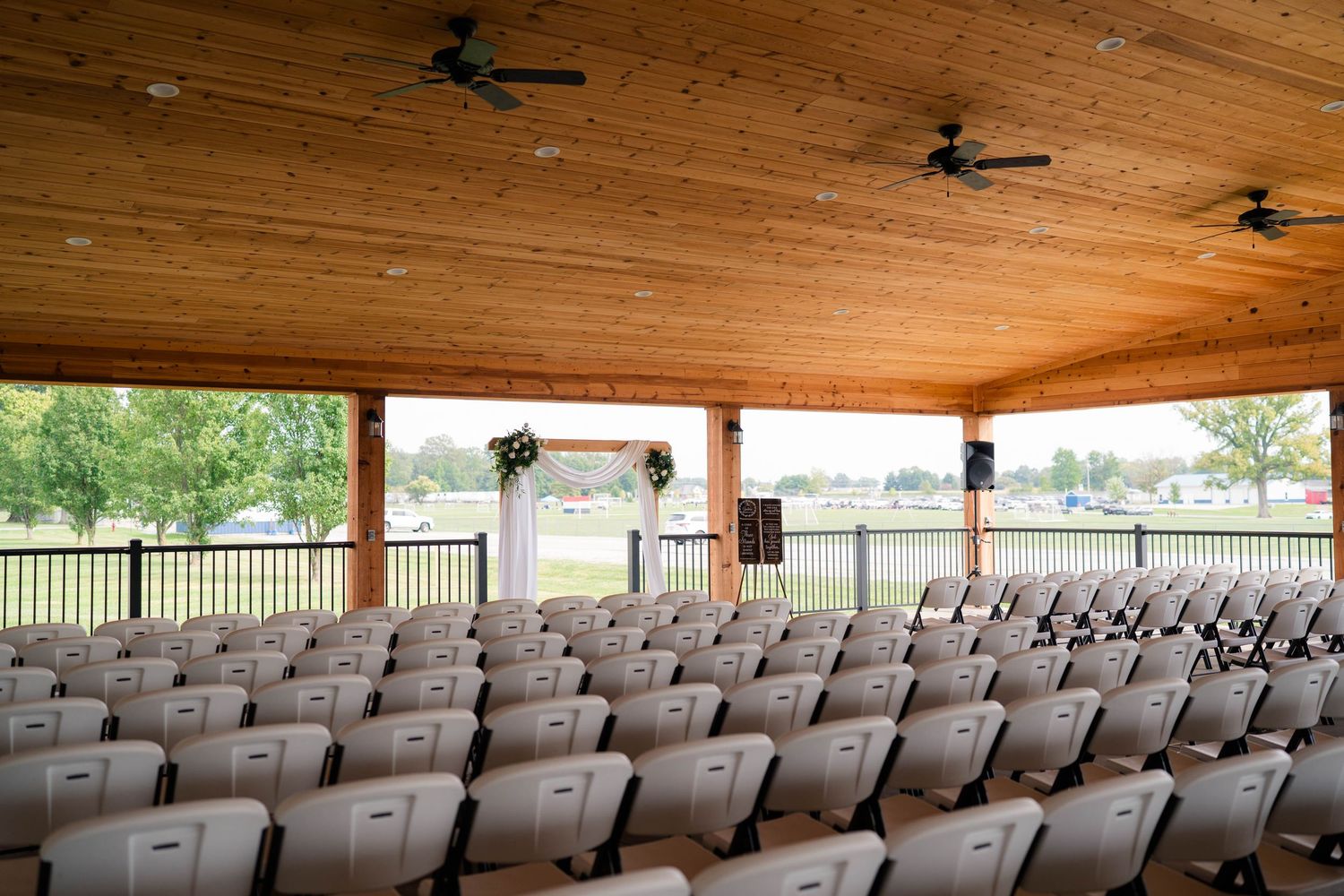 Outdoor wedding ceremony pavilion with rows of gray chairs facing a floral arch altar with scenic views.