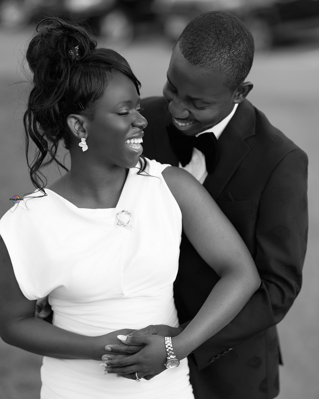 Black and white photo of a joyful bride in white dress and groom in tuxedo sharing a romantic moment.