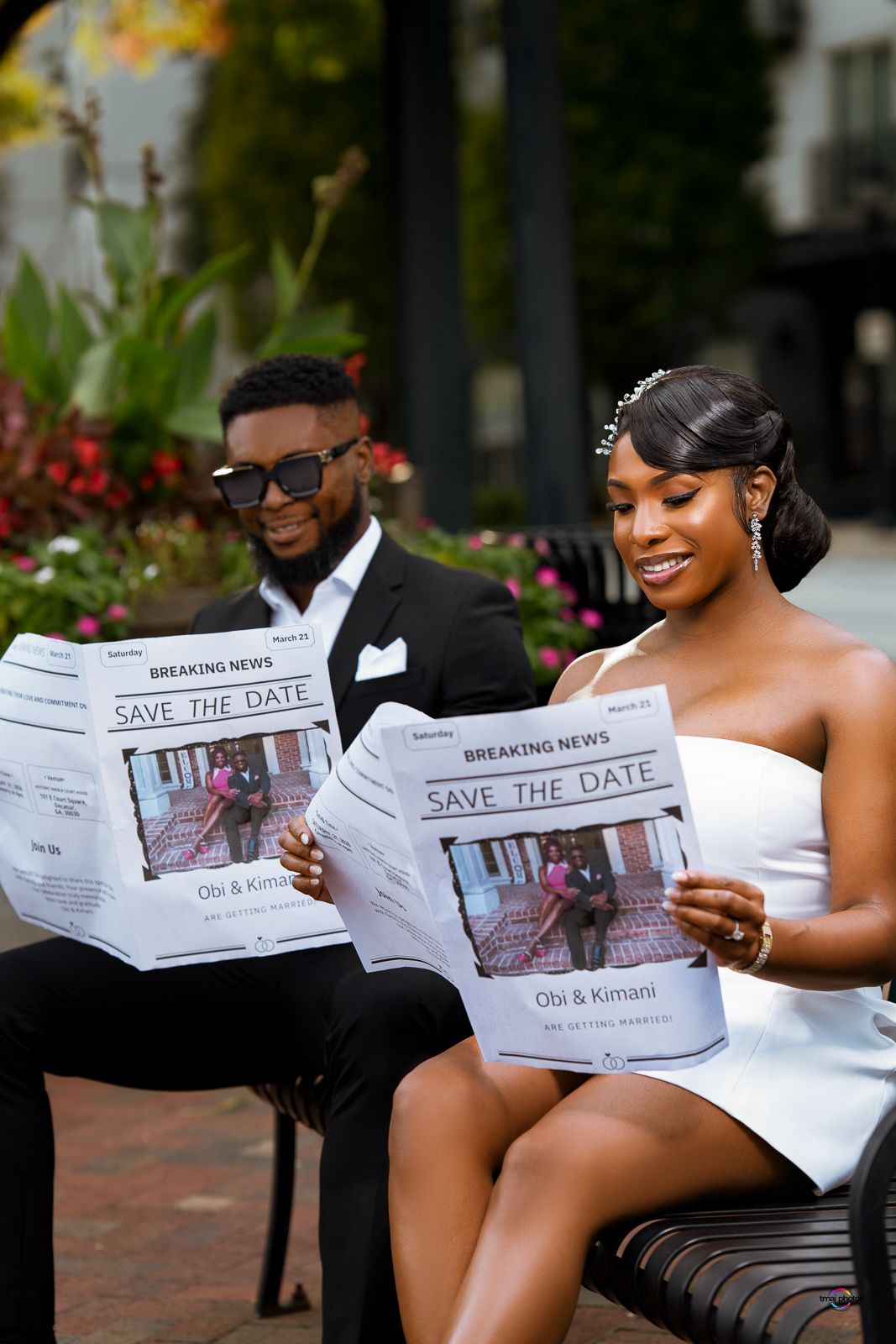 Couple in formal wear reading Save the Date newspapers outdoors, bride in white dress and groom in black tuxedo.