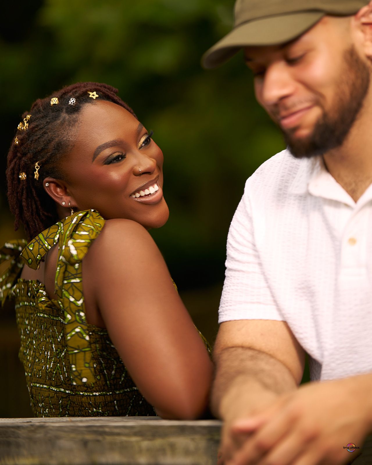 A smiling woman in a gold sequin dress with star hair pins laughs beside a man in a white polo outdoors.