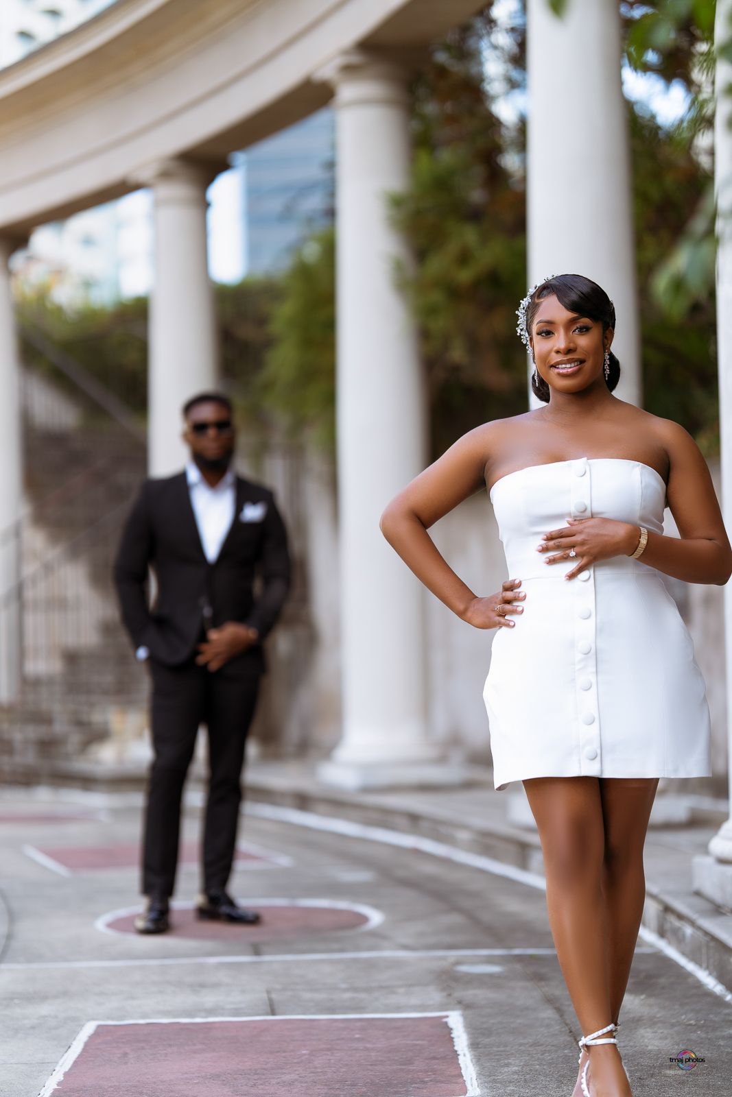 Woman in white strapless mini dress posing near classical columns.
