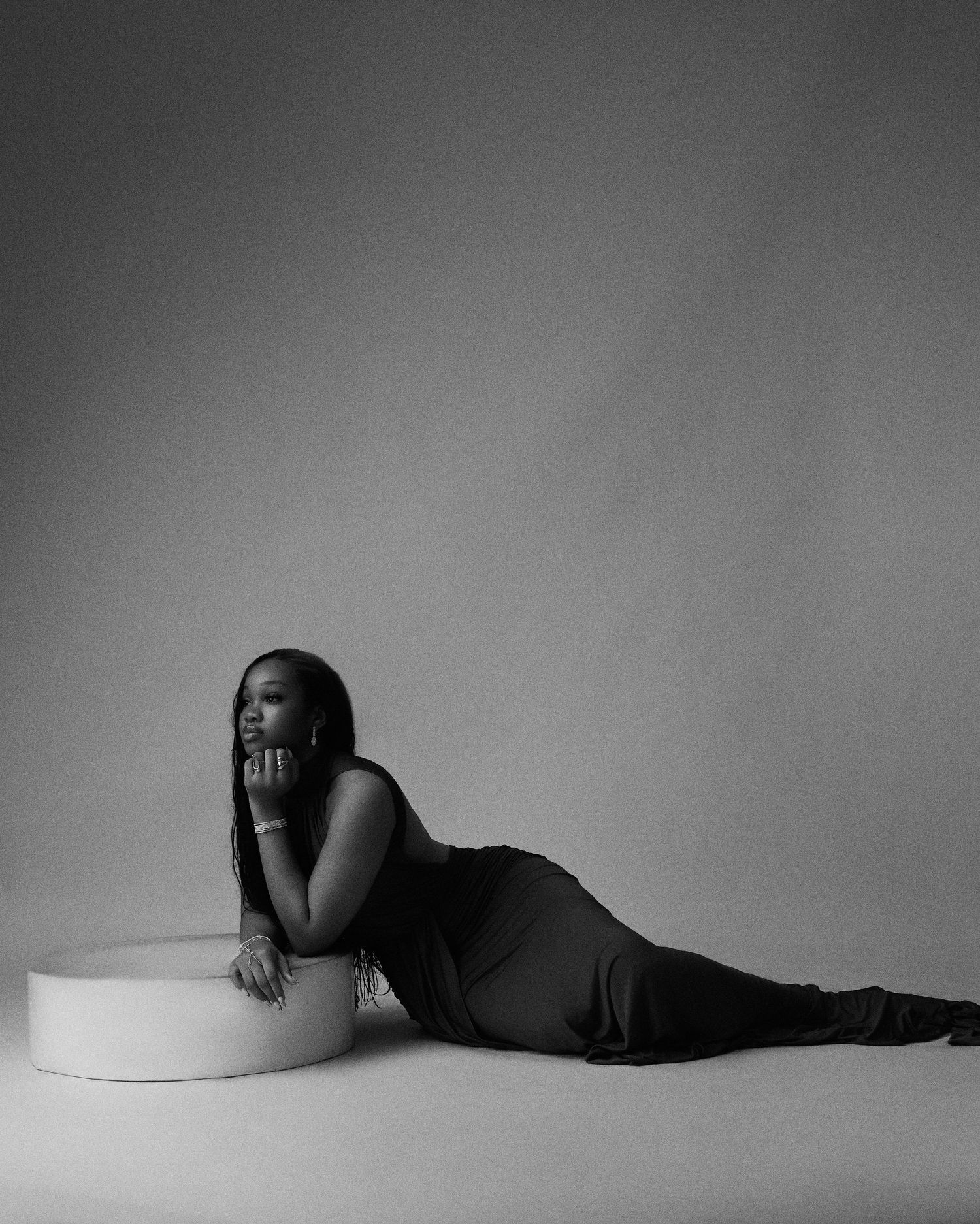 Black and white photo of woman in sleek dress posing on studio floor.