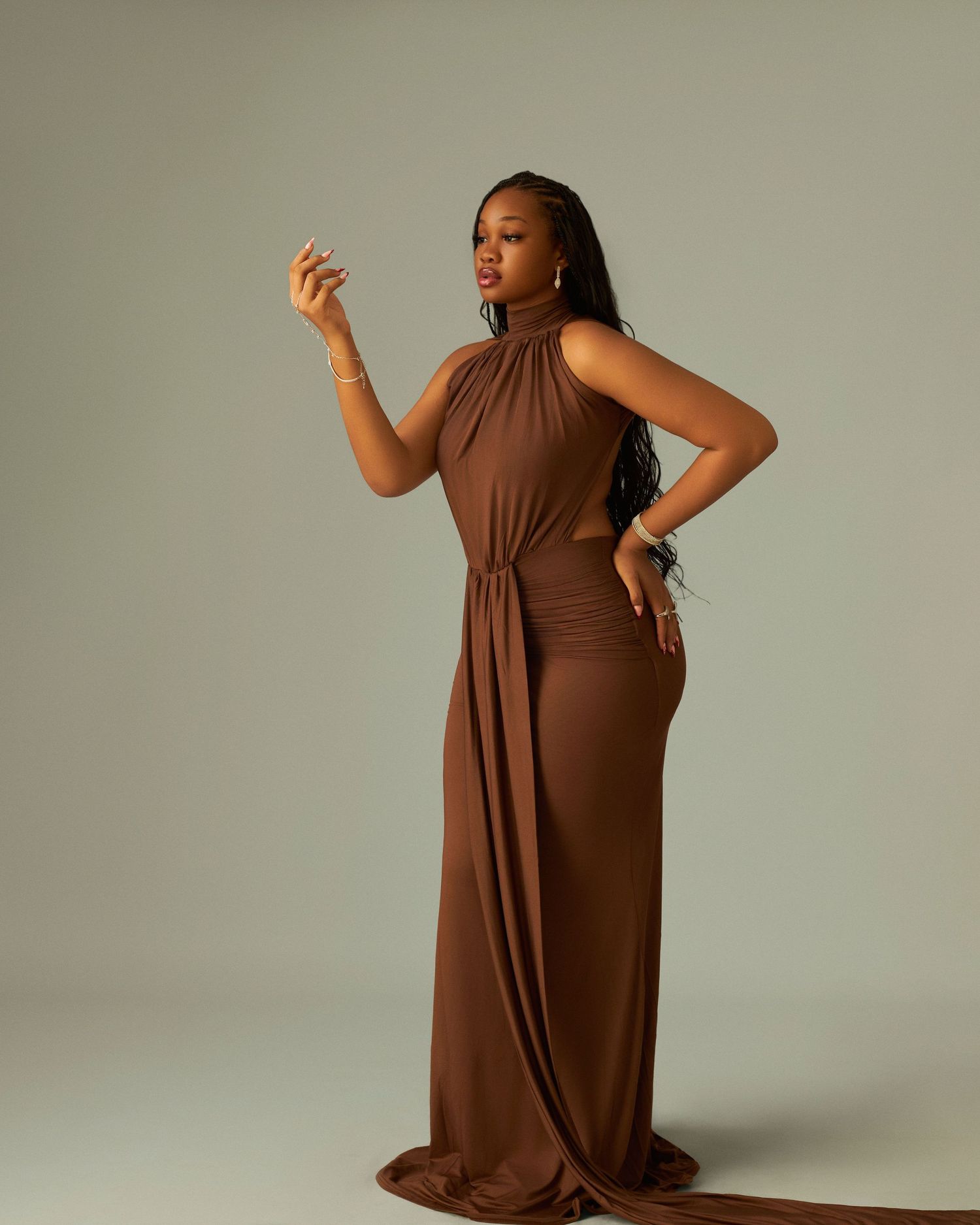 Woman in elegant brown halter maxi dress posing gracefully in studio.