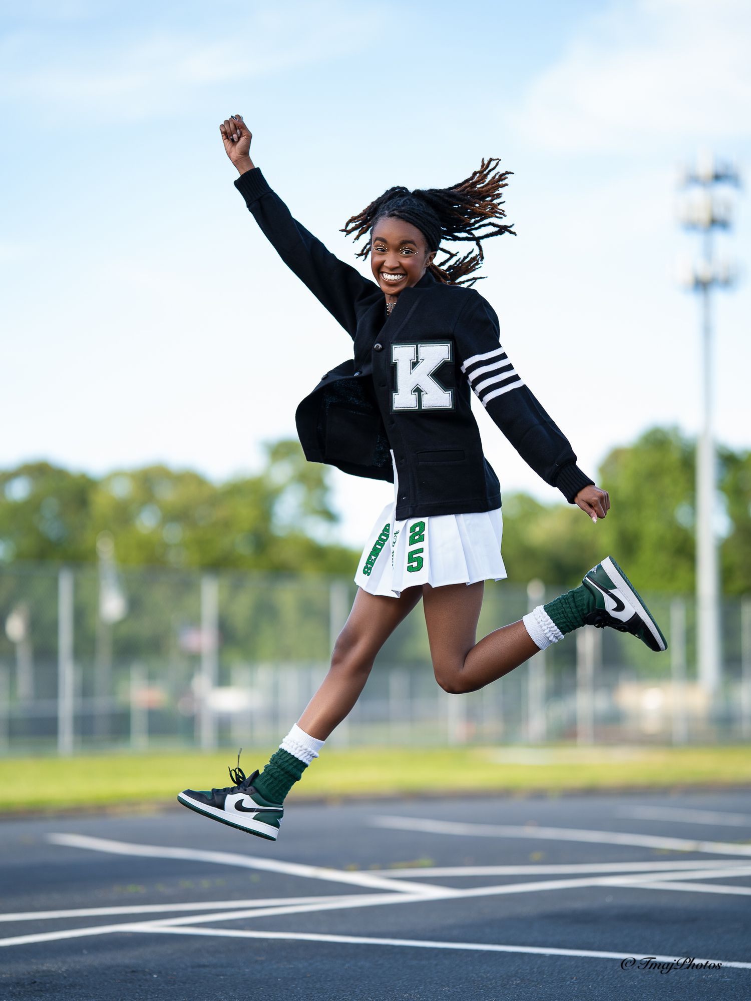 Student jumping on track in black letterman jacket and white skirt.
