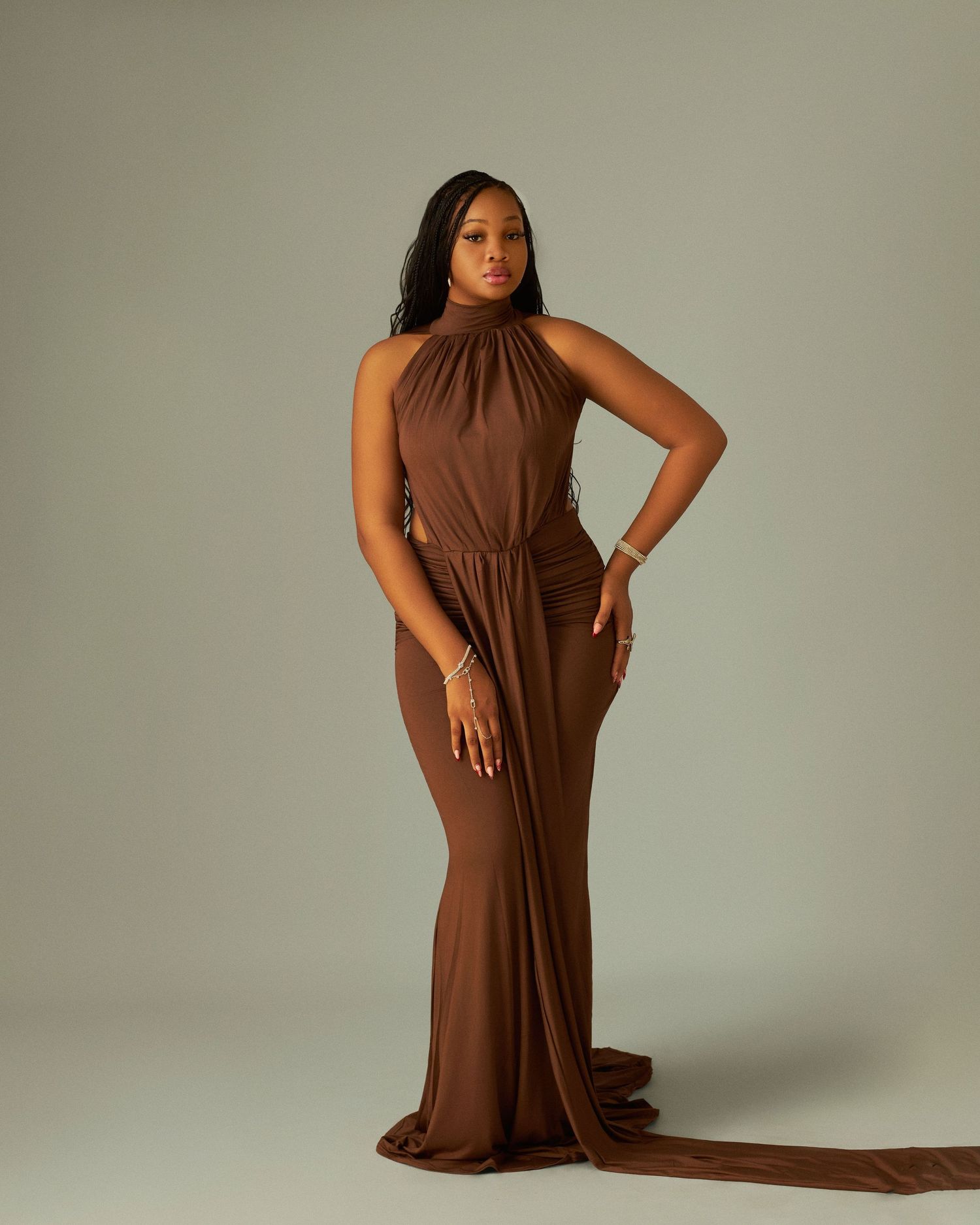 Woman in elegant brown halter neck maxi gown posing gracefully in a professional studio setting.
