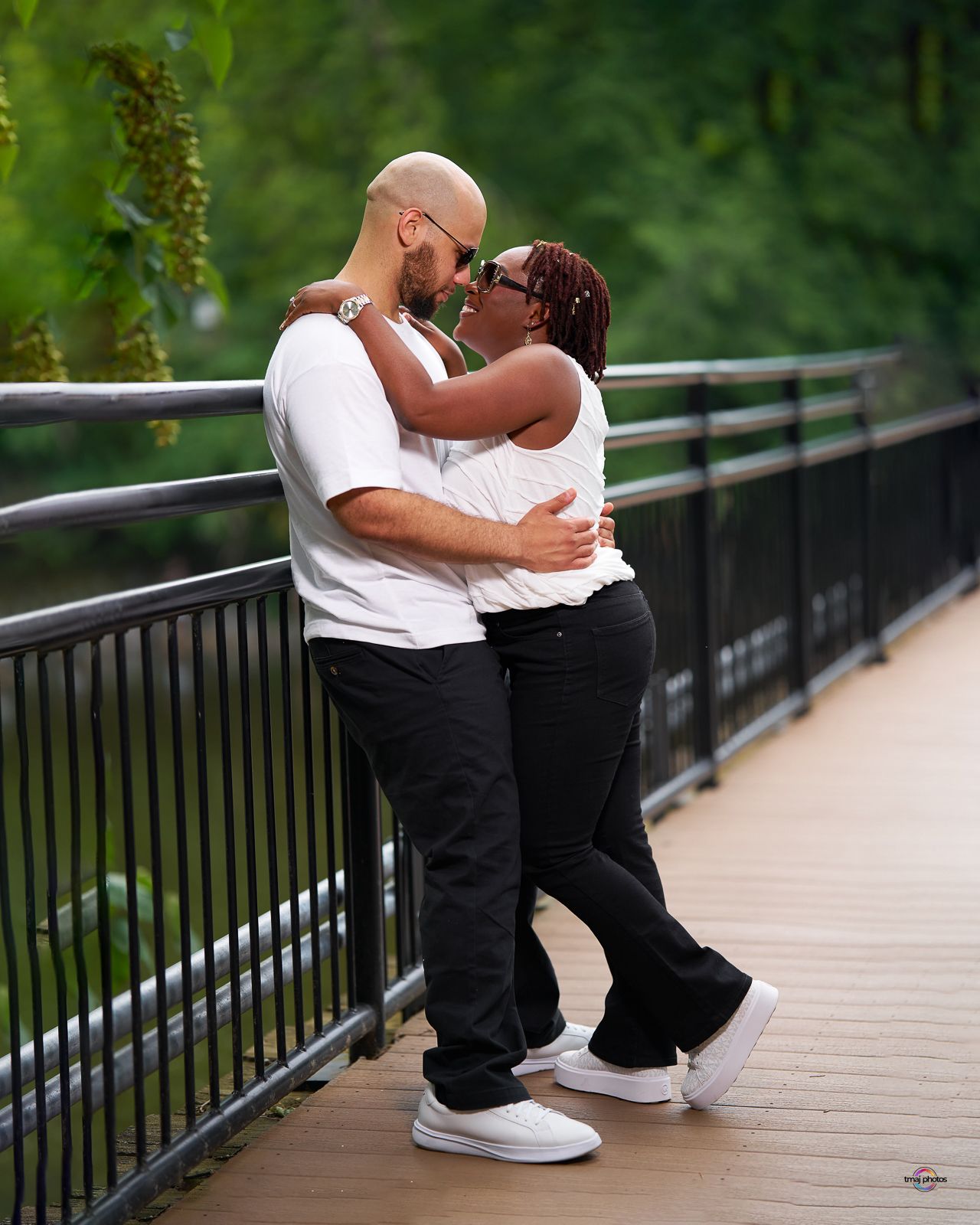A couple shares a romantic moment on a wooden bridge, dressed in matching white tops and black pants.