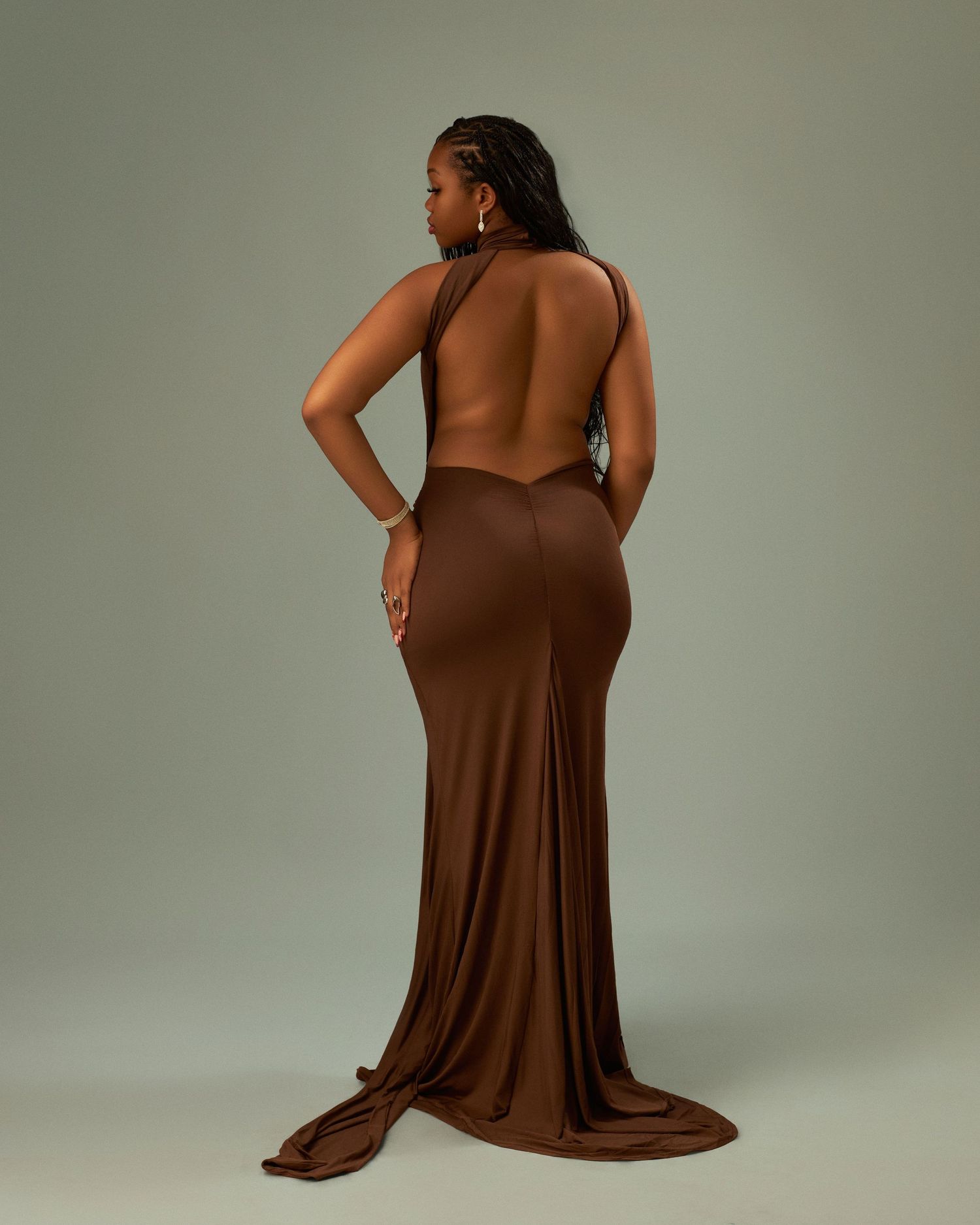 Woman in backless brown halter gown with train, posing gracefully against neutral backdrop.