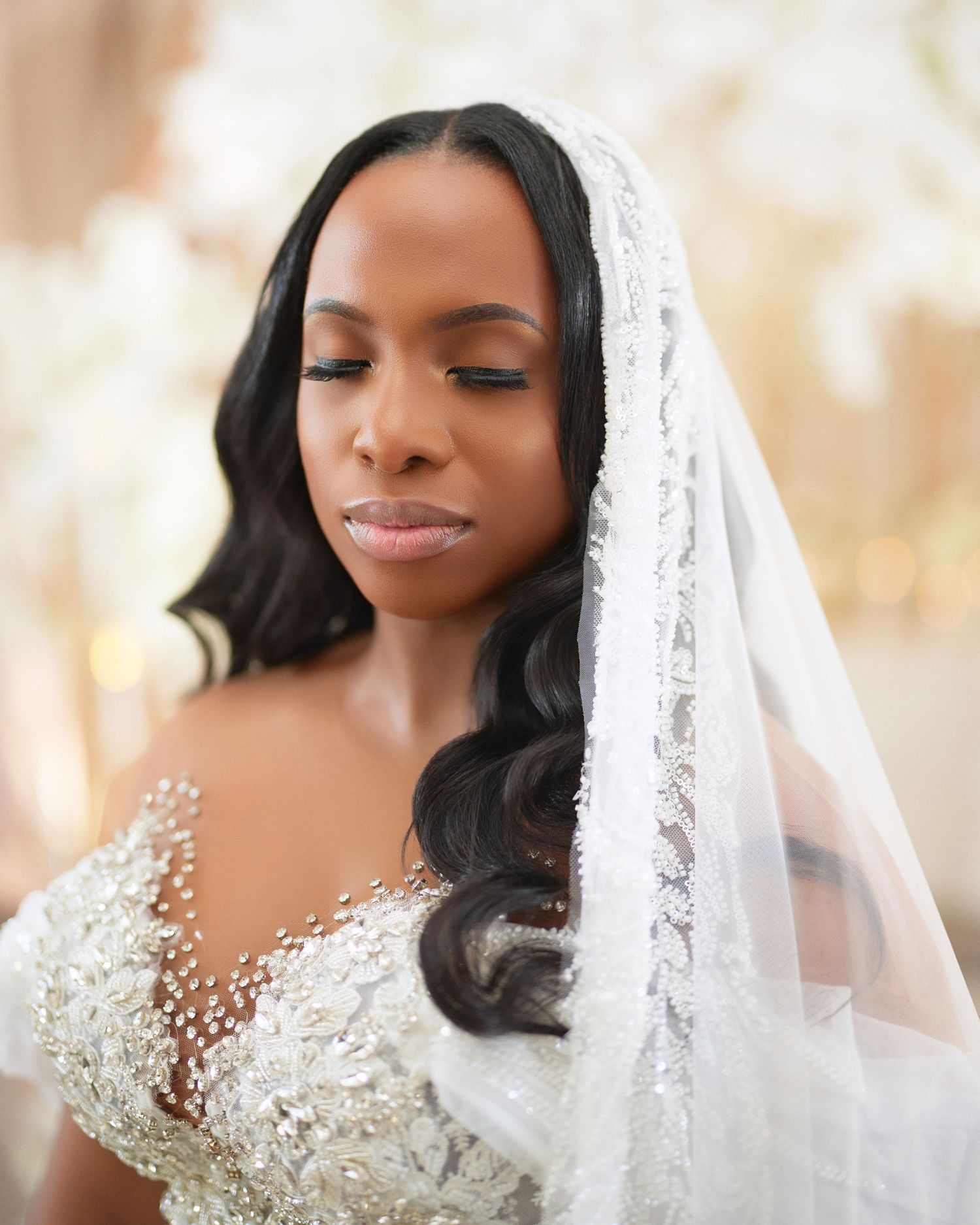 Elegant Black bride wearing a beaded white wedding gown and lace veil, eyes closed in a serene moment.