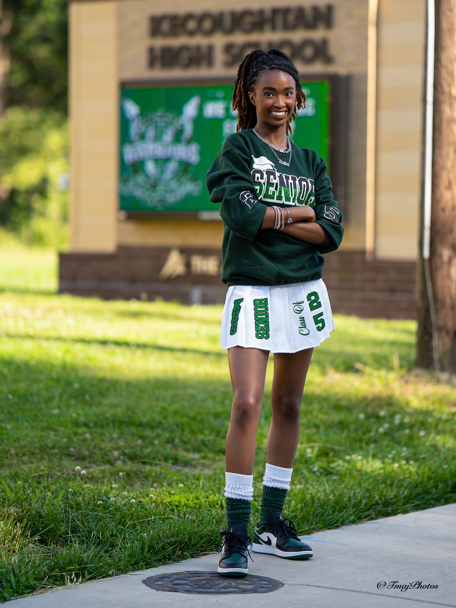 Young woman in green Kecoughtan High School athletic outfit posing by school sign outdoors.