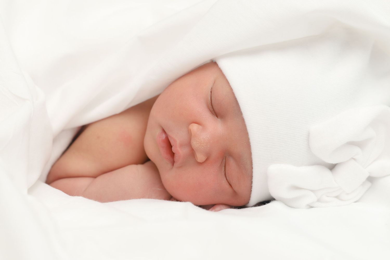 Peaceful newborn baby sleeping in a white hat and soft white blanket.
by Andrew Fein Photography - Family and Newborn Photo