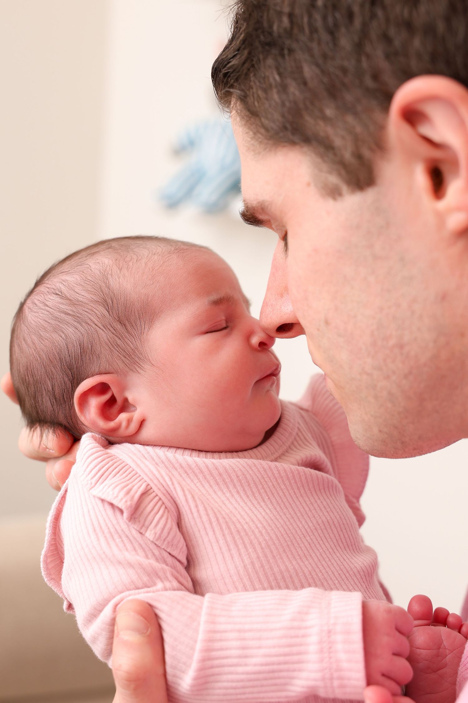 A father tenderly touches noses with his newborn baby girl dressed in pink, sharing a precious bonding moment.