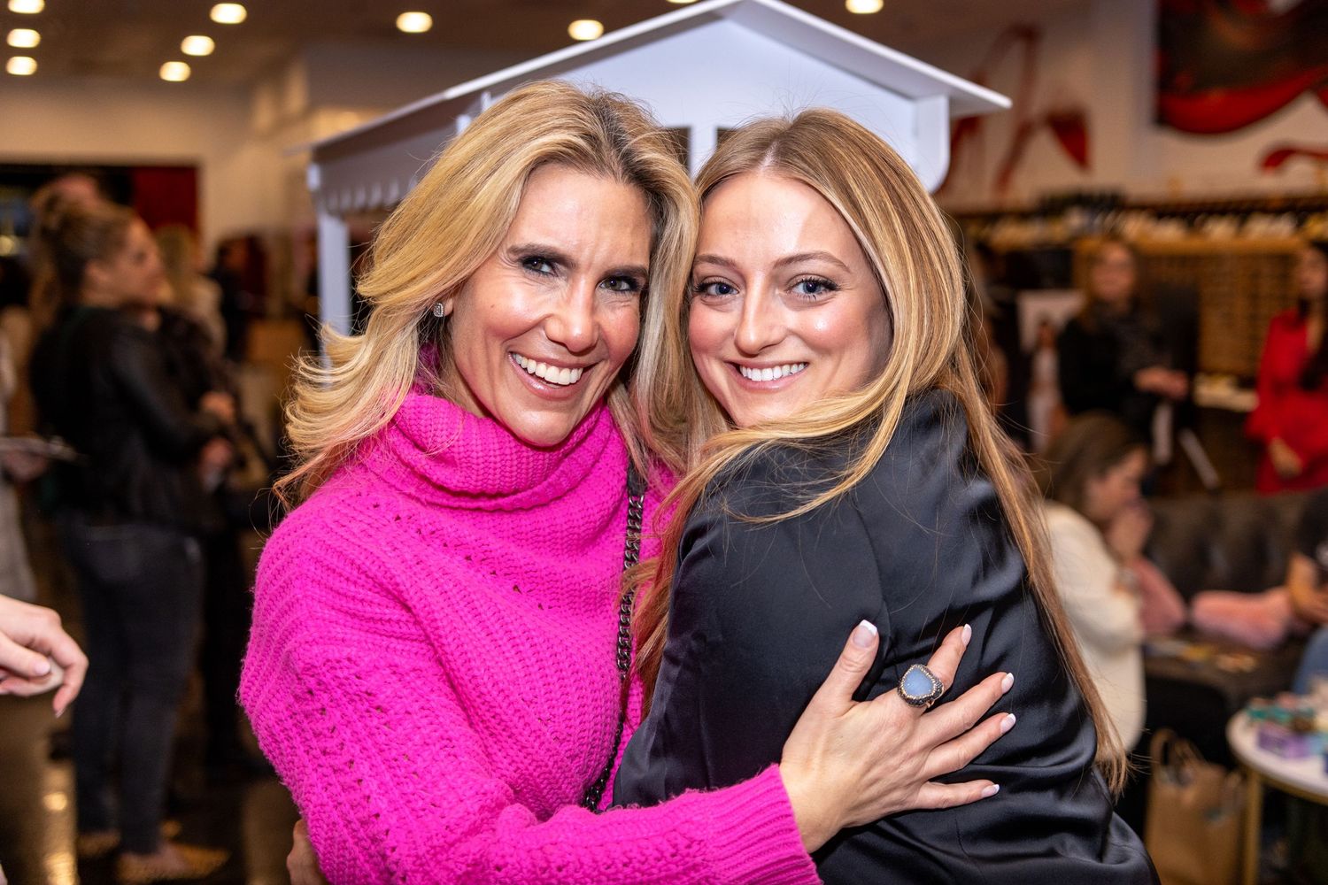 Two smiling women hugging at a busy indoor retail store event.
by Andrew Fein Photography - Family and Newborn Photo