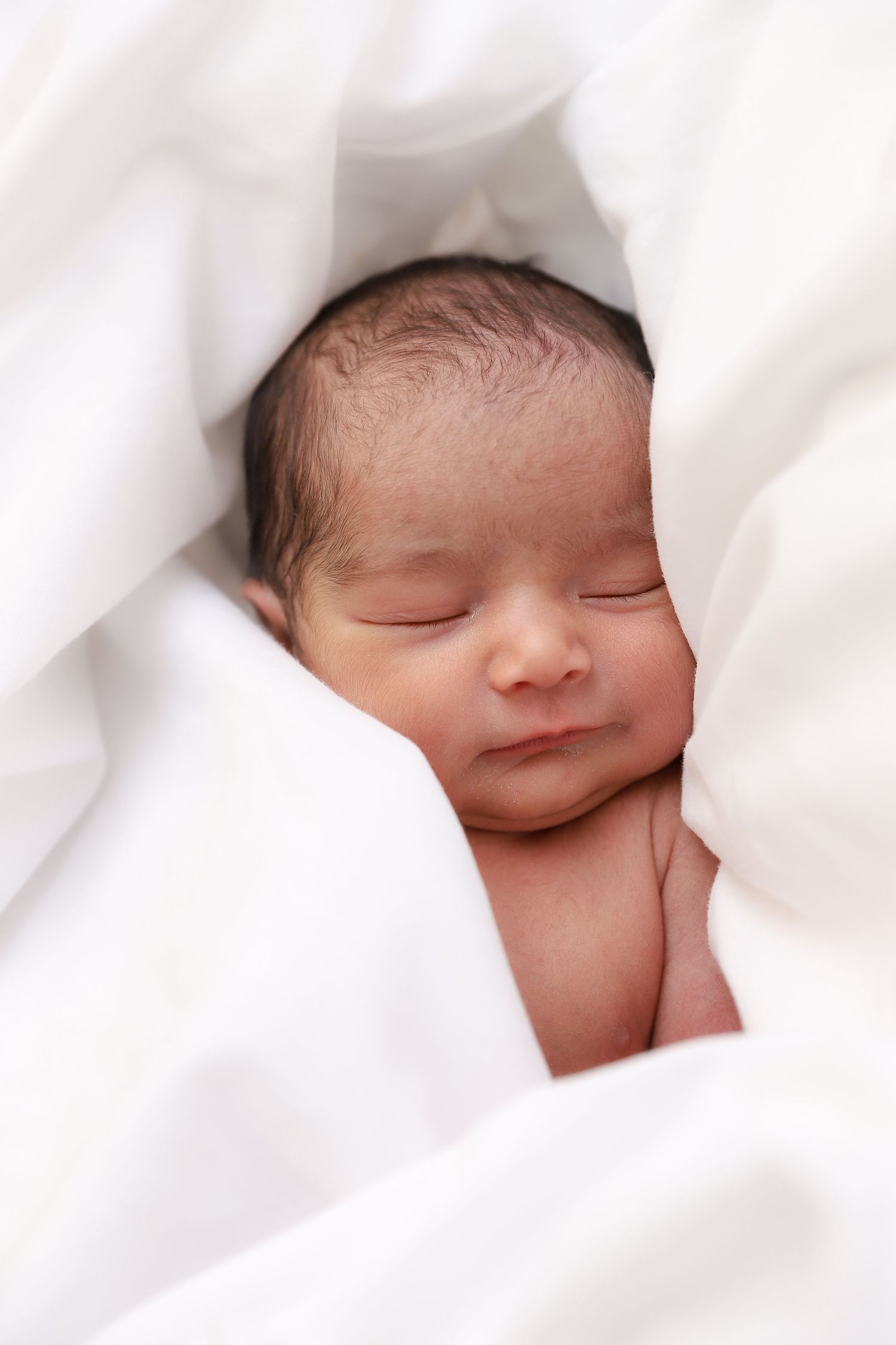 Serene newborn baby sleeping peacefully nestled in soft white fabric folds.
by Andrew Fein Photography - Family and Newborn Photo