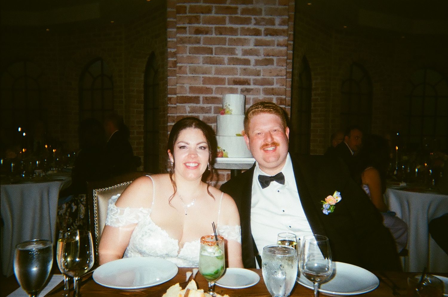 Happy bride and groom smile at their wedding reception dinner table with a white cake backdrop.
by Andrew Fein Photography - Family and Newb