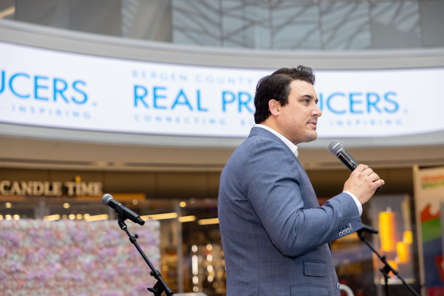 Man in a gray suit speaking at a podium inside a shopping mall at a business event.
by Andrew Fein Photography - Family and Newborn Photo