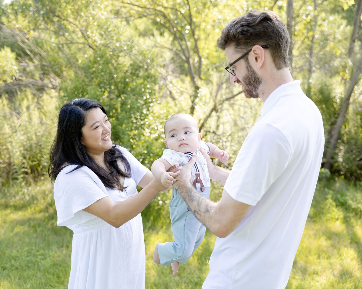 Happy young family with mother, father, and baby enjoying outdoor time together in a lush green park setting.