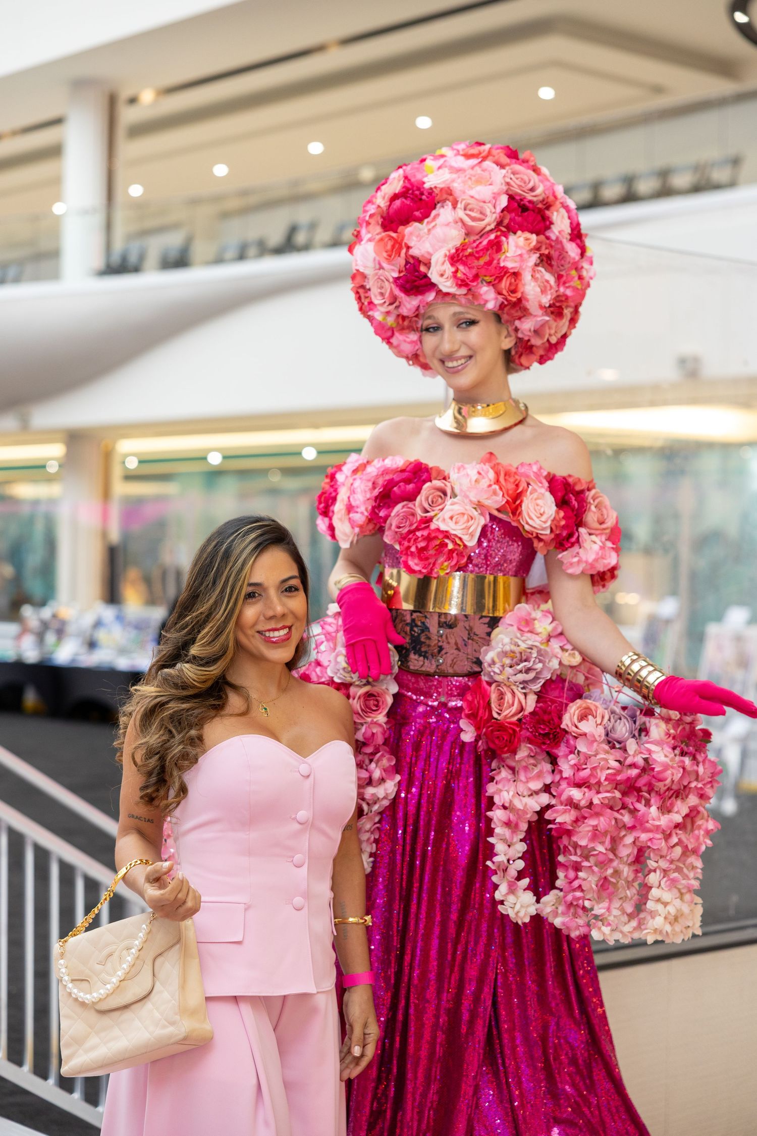 Woman in pink outfit posing with a tall floral costume performer at a mall event.by Andrew Fein Photography - Family and Newborn Photo