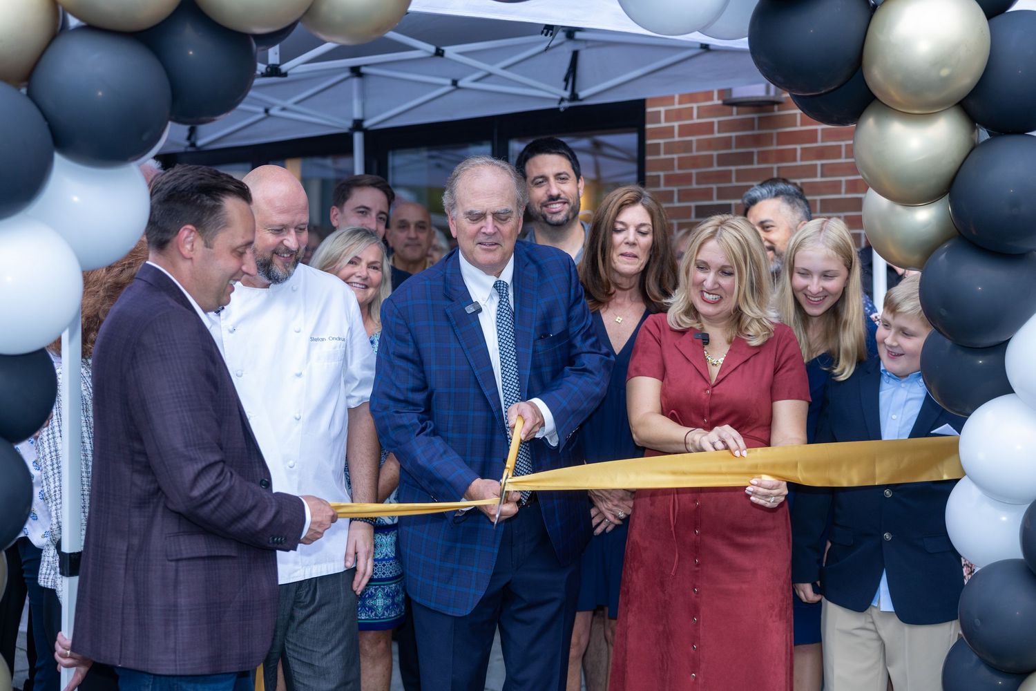 Business owners cutting gold ribbon at grand opening under balloon arch.
by Andrew Fein Photography - Family and Newborn Photo