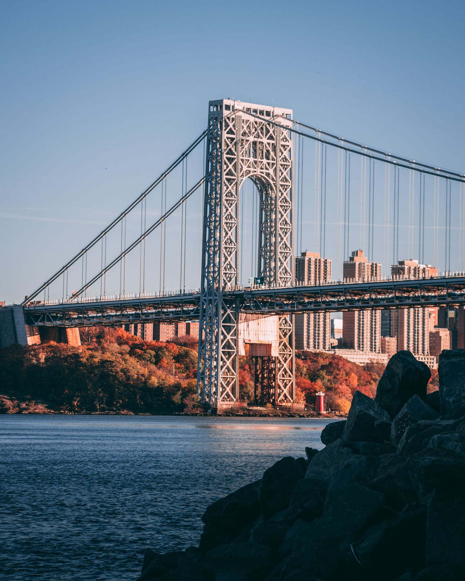 George Washington Bridge spanning the Hudson River with autumn foliage and NYC skyline in the background on a clear day.