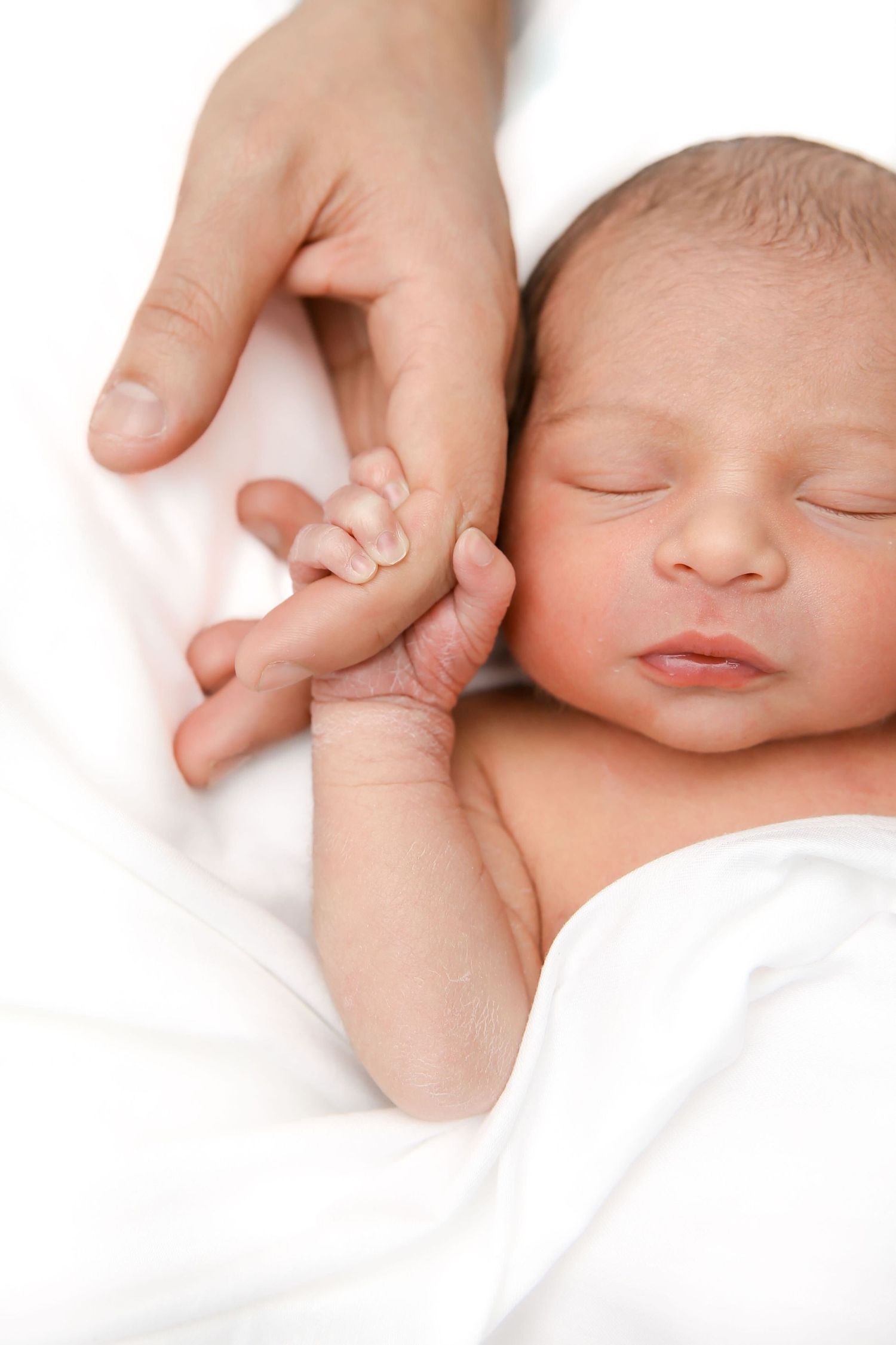 Sleeping newborn baby gently holding an adult finger on a white blanket.
by Andrew Fein Photography - Family and Newborn Photo