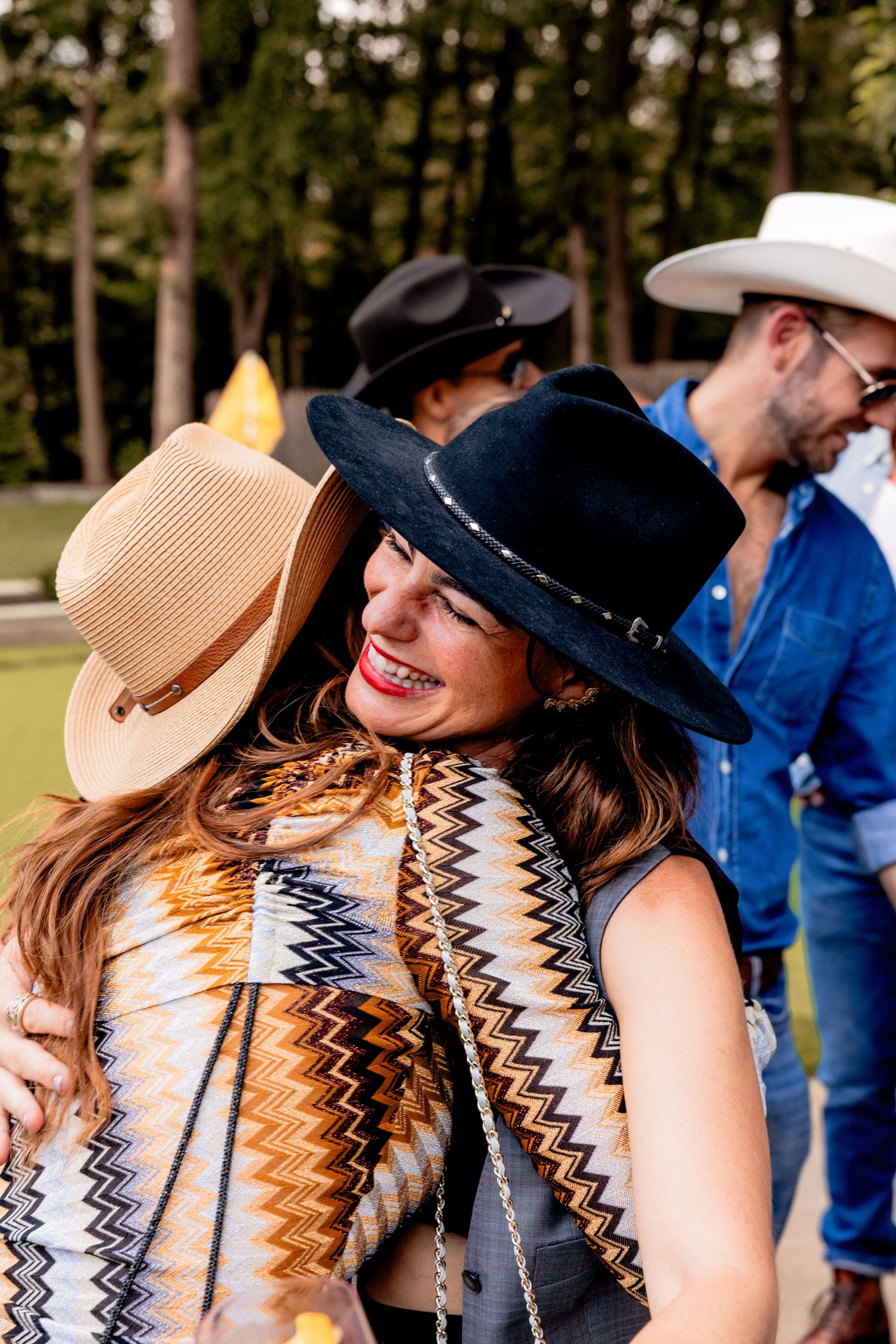 Two women wearing wide-brim hats hugging and smiling at outdoor event.
by Andrew Fein Photography - Family and Newborn Photo