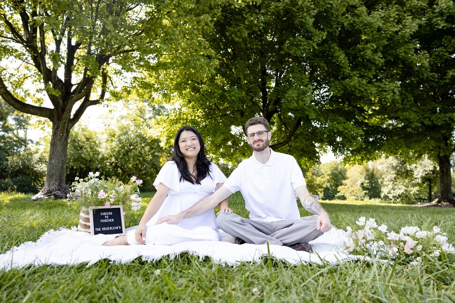 Smiling couple sits on a blanket in a park holding a pregnancy announcement letterboard sign.
by Andrew Fein Photography - Family and Newbor