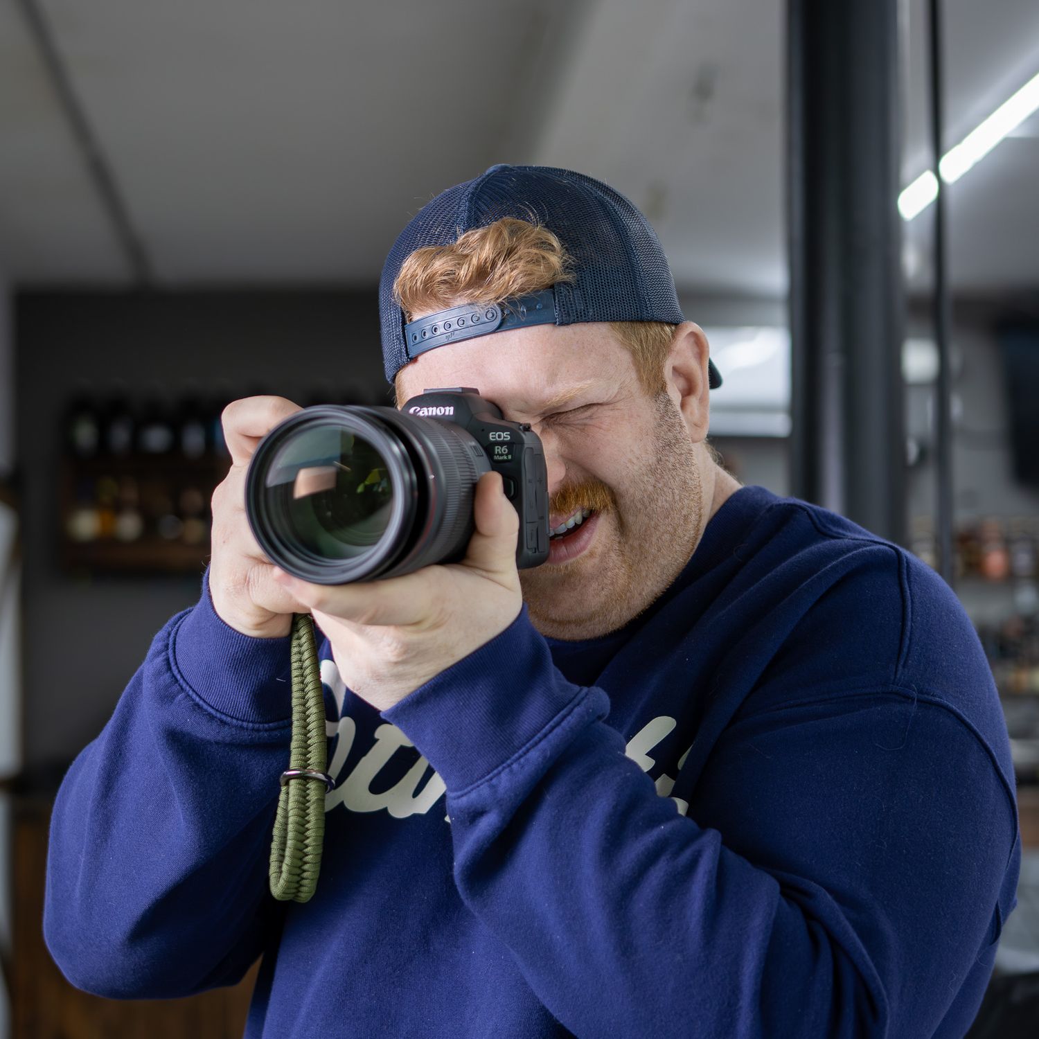 Smiling man with red beard wearing blue hoodie and cap, photographing with a mirrorless camera indoors.
by Andrew Fein Photography - Family