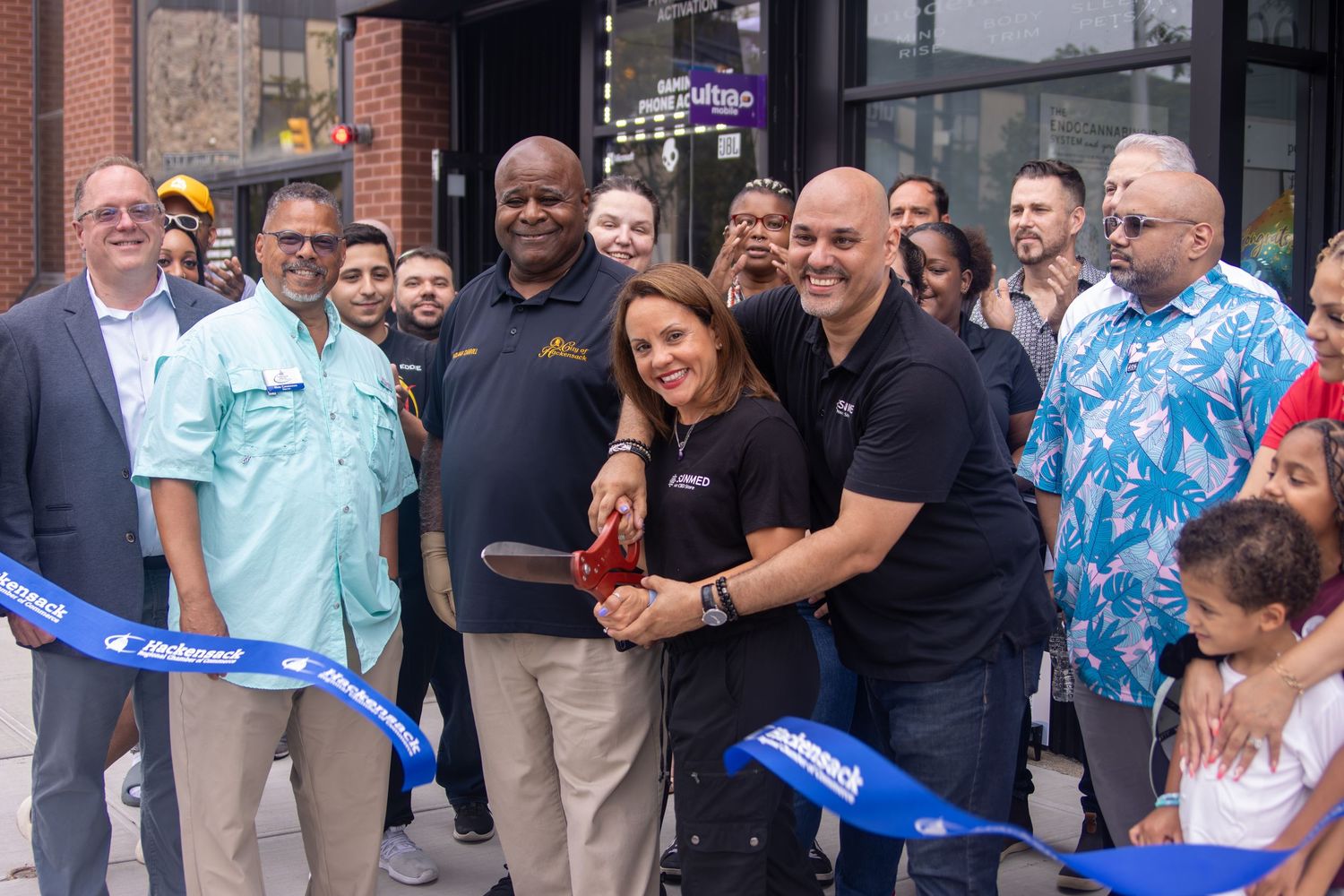Group of people cutting a blue ribbon at a grand opening ceremony outside a business.
by Andrew Fein Photography - Family and Newborn Photo