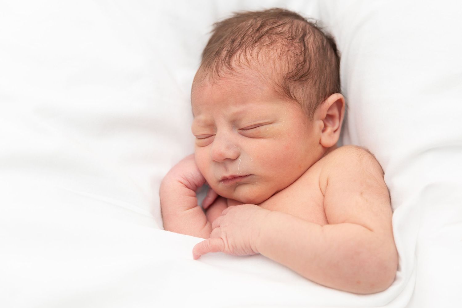 Newborn baby sleeping on a white blanket with hand tucked under chin.
by Andrew Fein Photography - Family and Newborn Photo