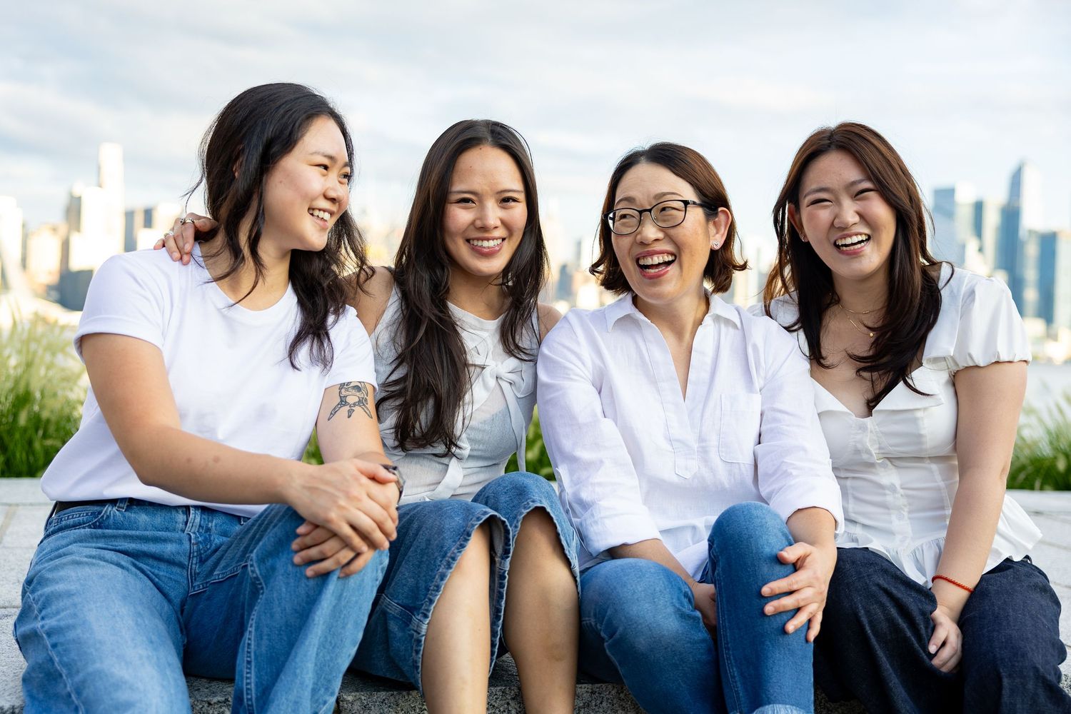 Four smiling Asian women sitting together outdoors with a city skyline in the background.
by Andrew Fein Photography - Family and Newborn Ph