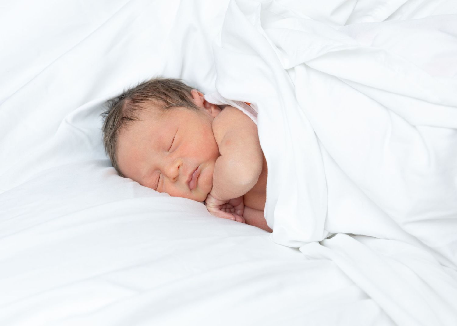 Peaceful newborn baby sleeping wrapped in soft white blankets on a white bed.
by Andrew Fein Photography - Family and Newborn Photo