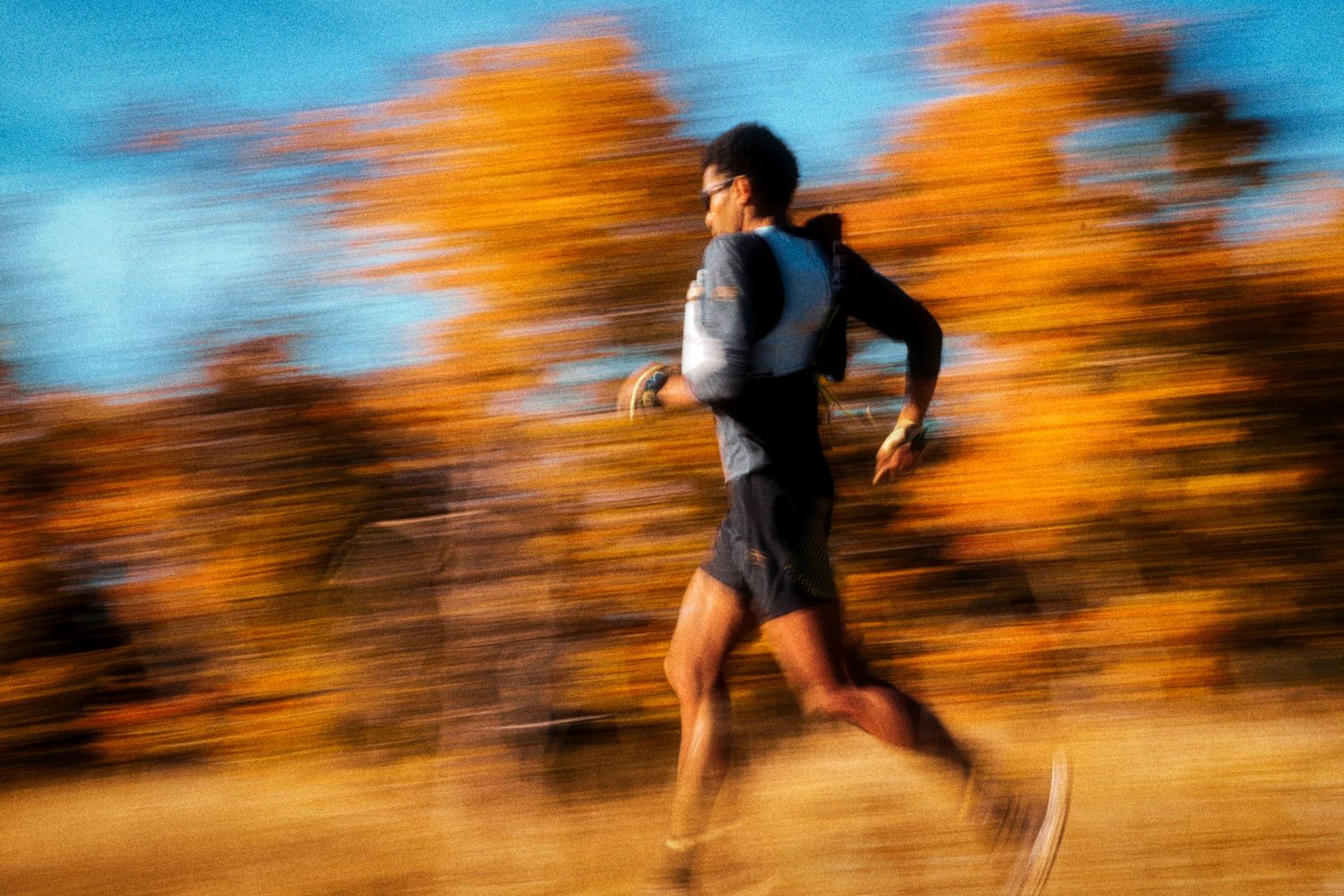 Man running outdoors in autumn, motion blur effect capturing speed among vibrant orange fall foliage.