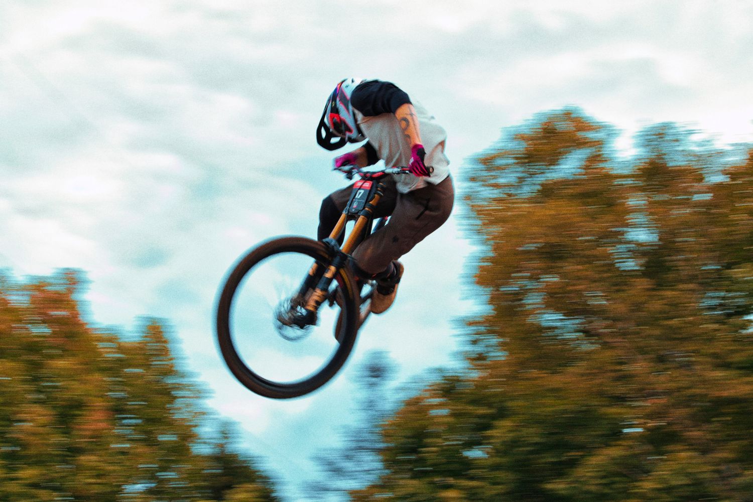 BMX rider performing a high jump trick against a cloudy sky with autumn trees in the background.