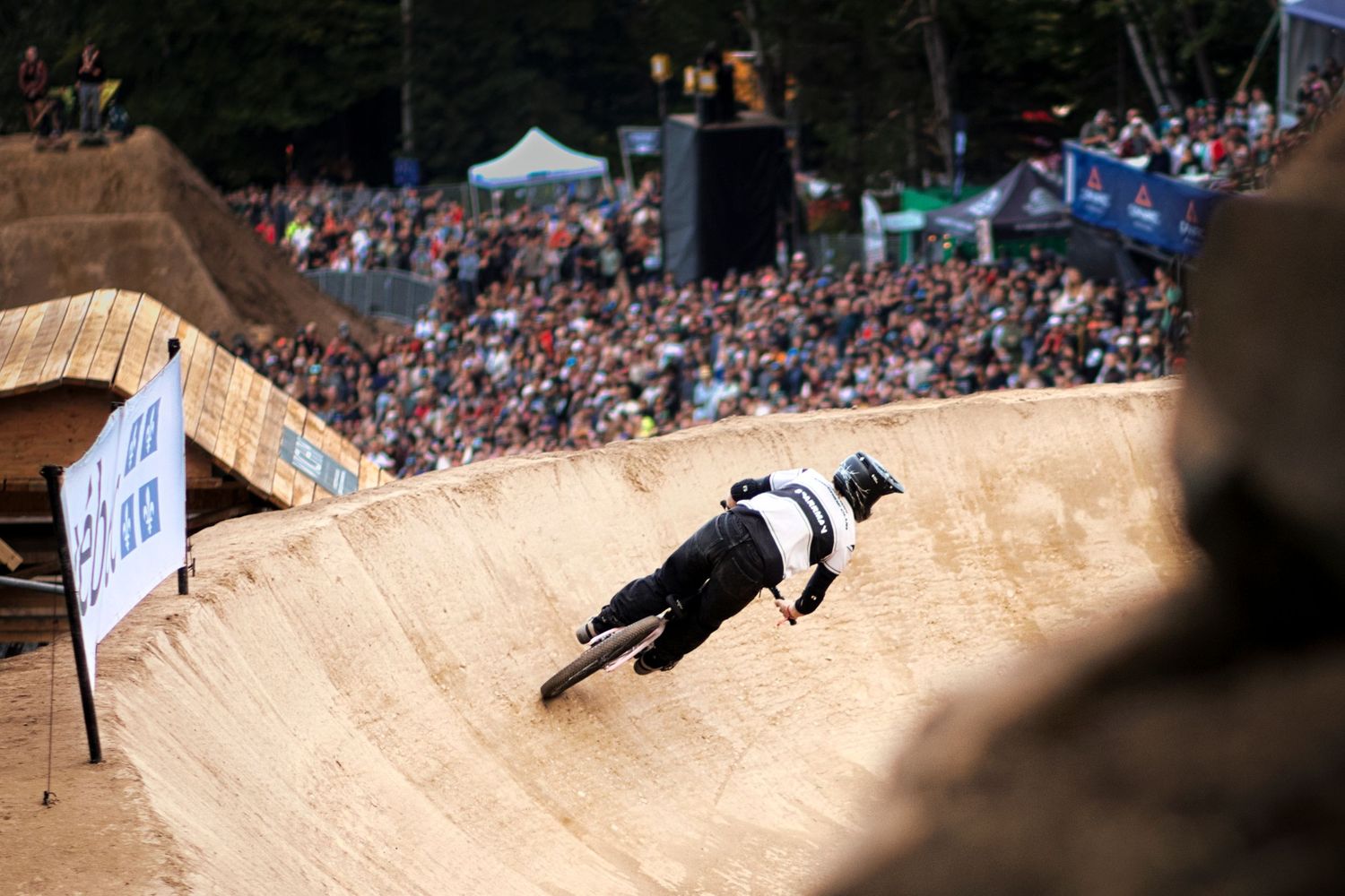 Mountain biker carving steep dirt berm at Red Bull event before massive cheering spectator crowd.