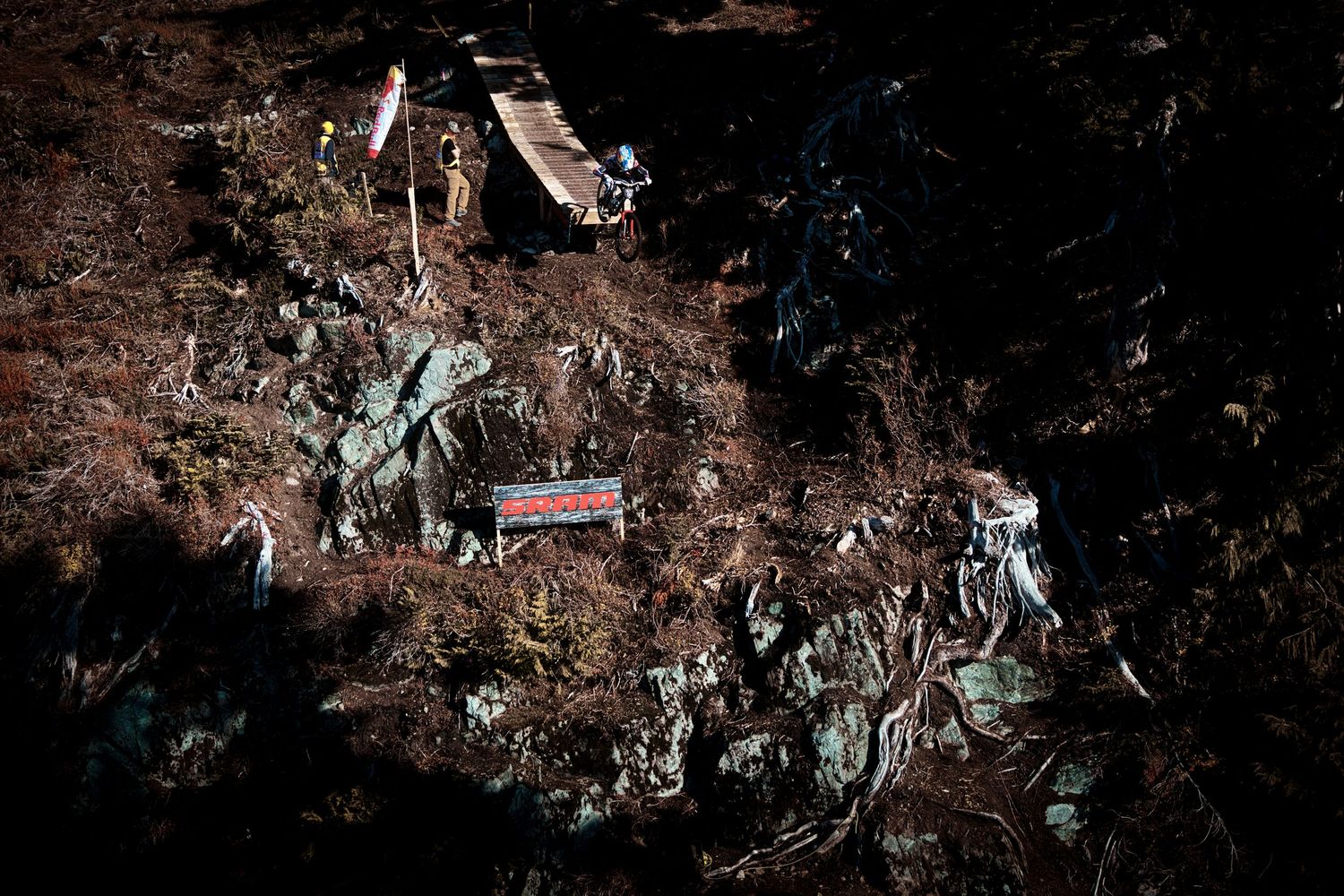 Aerial view of debris scattered across a dark, rugged hillside with a red-and-white sign and wreckage among brush and rocks.