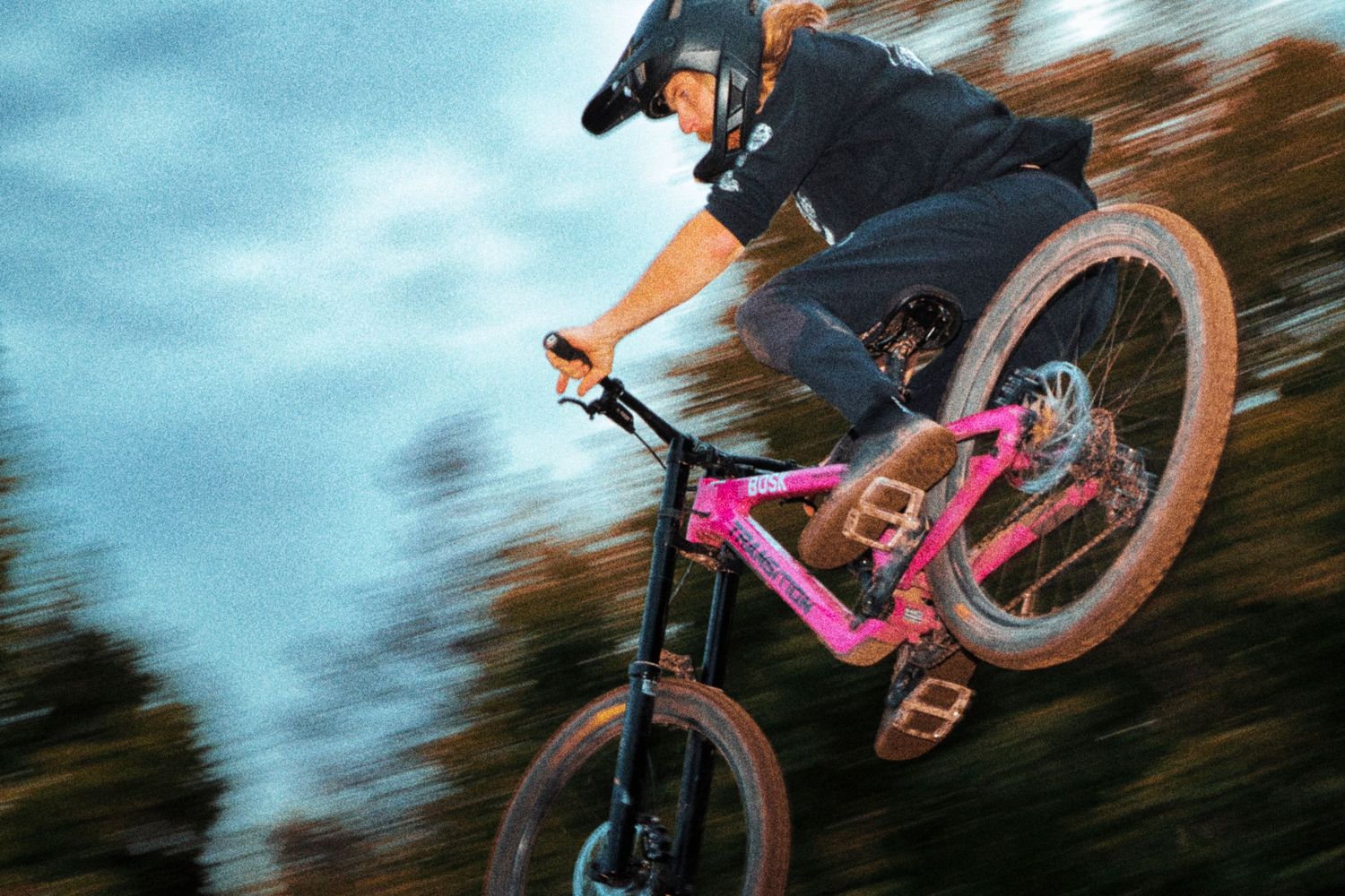Rider on pink Transition mountain bike captured mid-air with motion blur during whip off competition by Dave Clément, Québec.