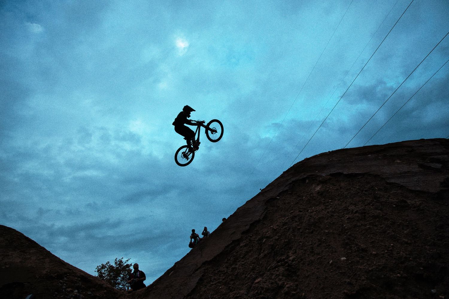 Silhouette of a mountain biker catching big air against a dramatic blue cloudy sky at dusk at Crankworx Mont-Sainte-Anne by Dave Clément.