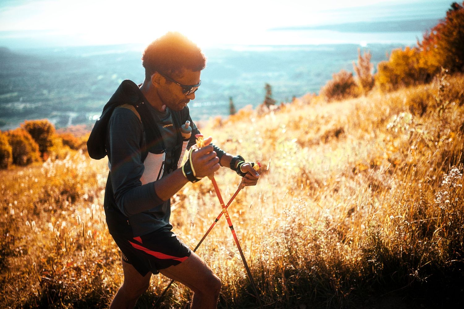 Hiker with trekking poles and backpack traversing a golden sunlit hillside trail during a scenic mountain adventure.